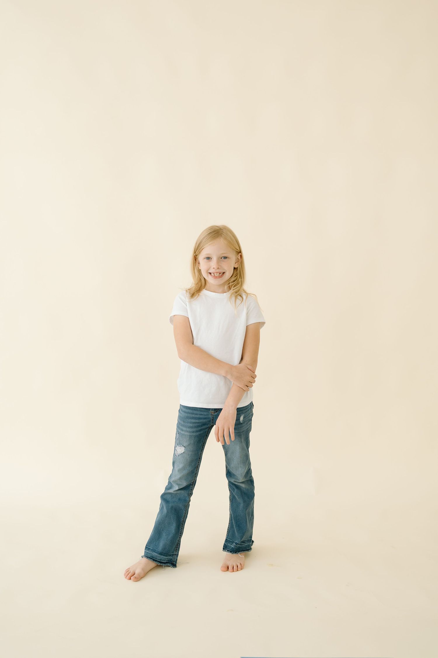 A child in blue jeans and white shirt poses playfully in four different stances against a cream colored backdrop.