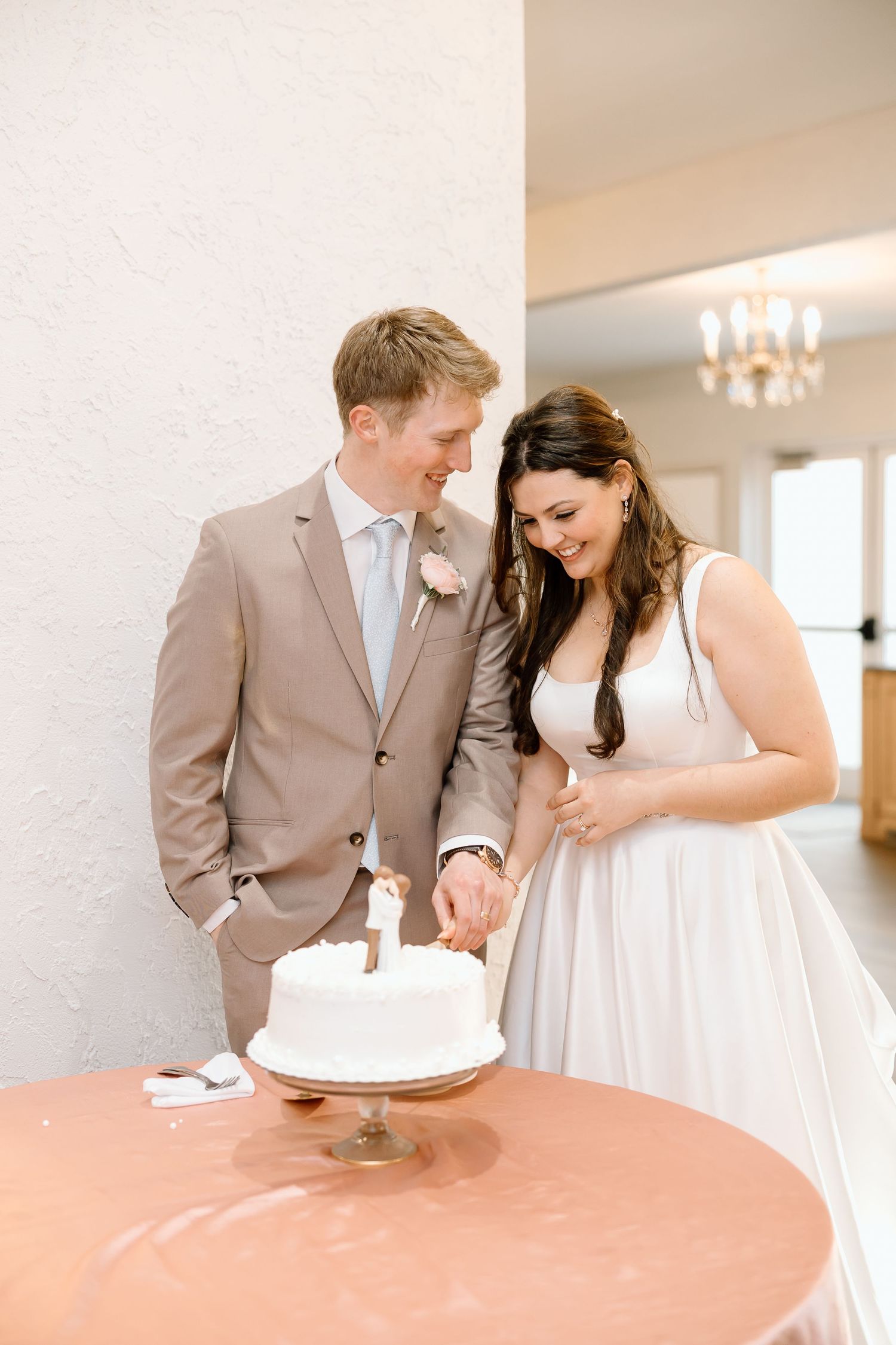 A couple in wedding attire shares an intimate moment while leaning against a wall in a bright indoor setting.