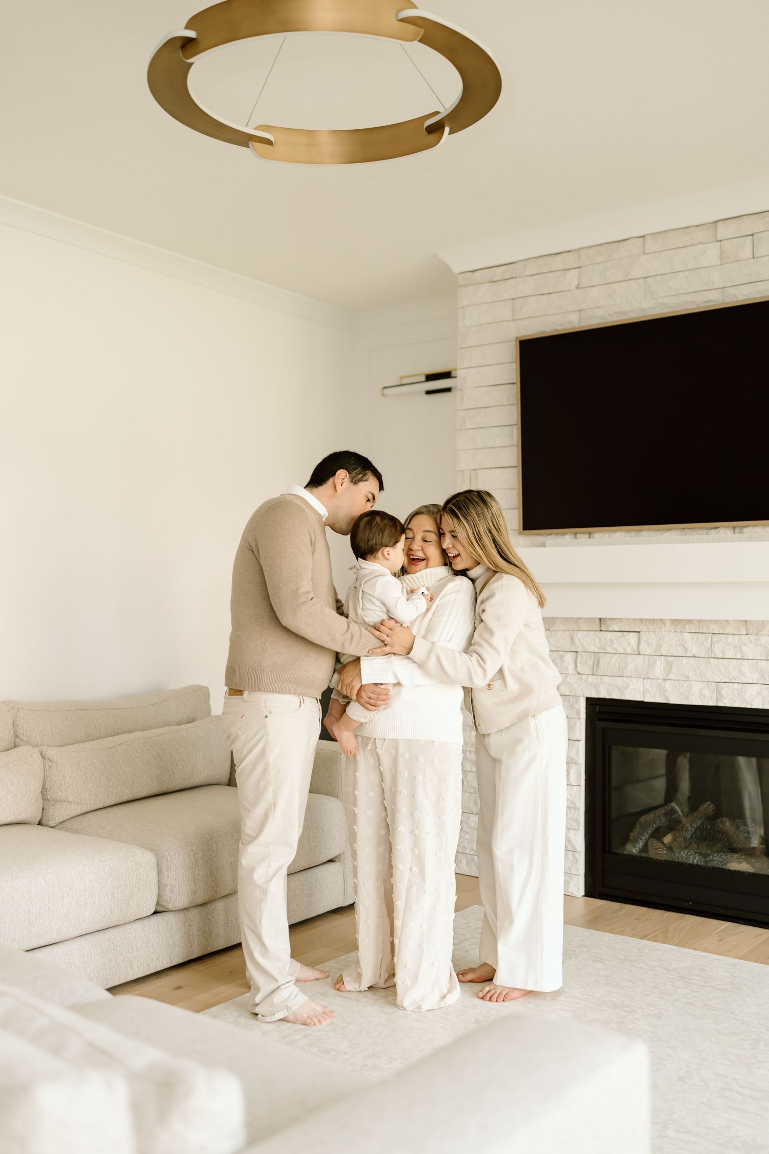 A family in white outfits shares tender moments together on a light-colored couch in a modern living room.