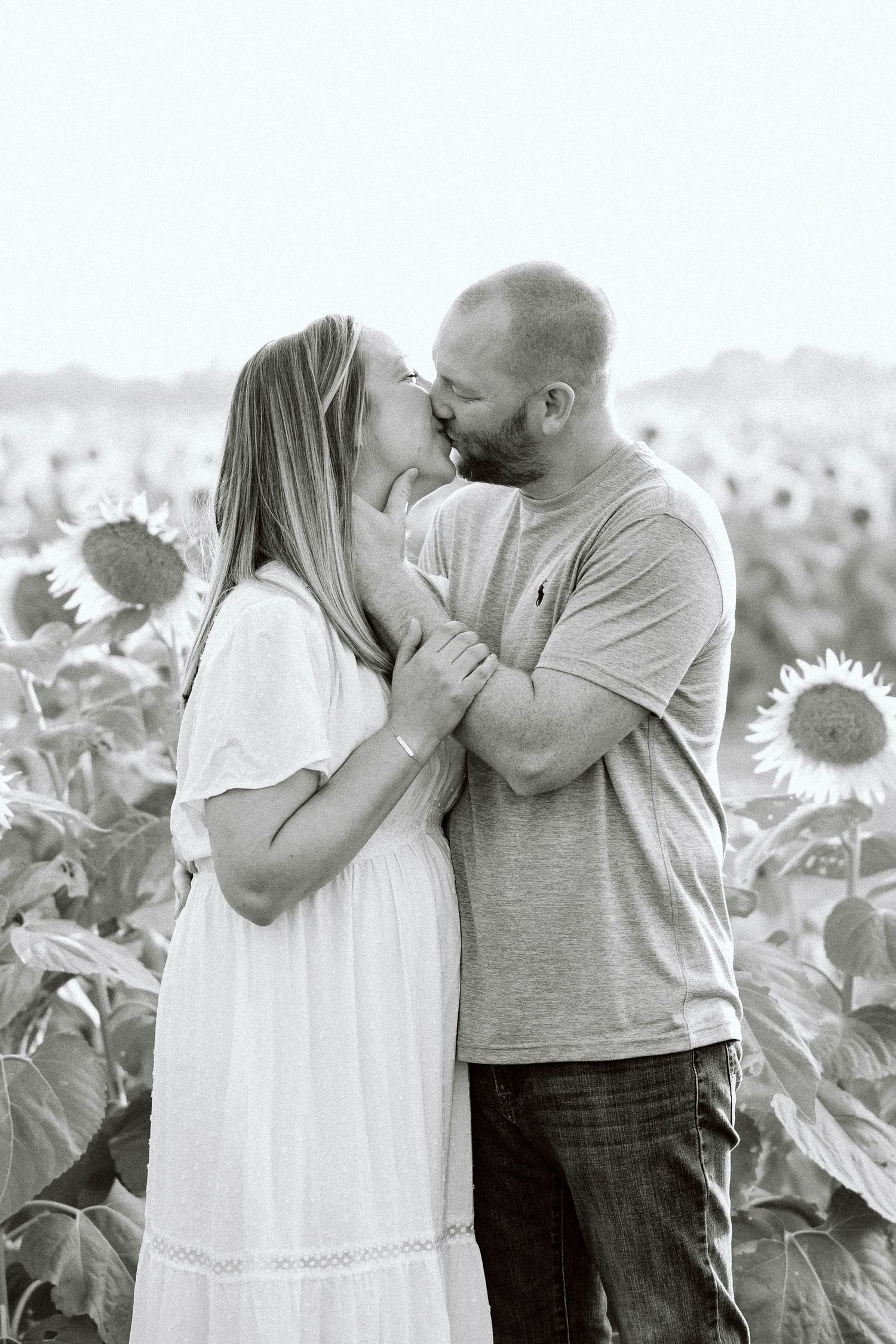 A romantic couple shares tender moments in a sunflower field, captured in black and white photography.
