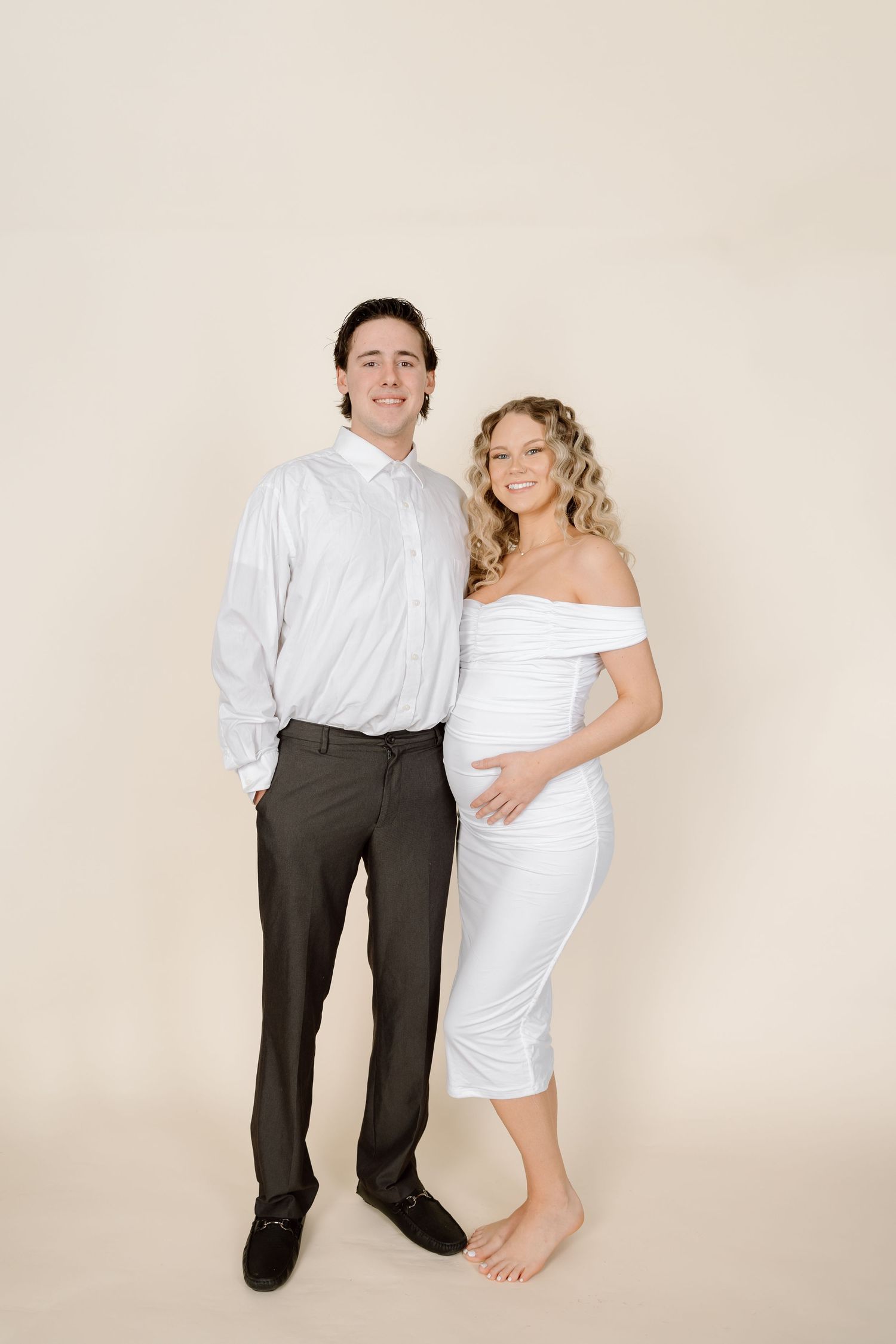 A series of four artistic maternity photos showing a couple in white and dark clothing against a neutral backdrop.