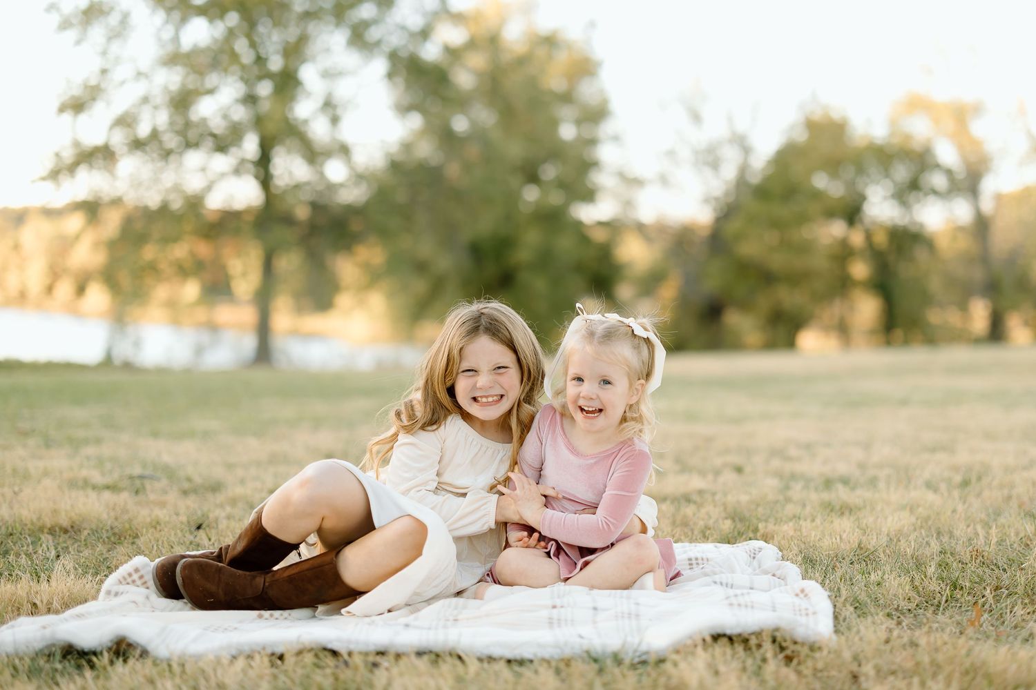 Children lying on a white blanket in a grassy field at sunset while laughing and playing together.
