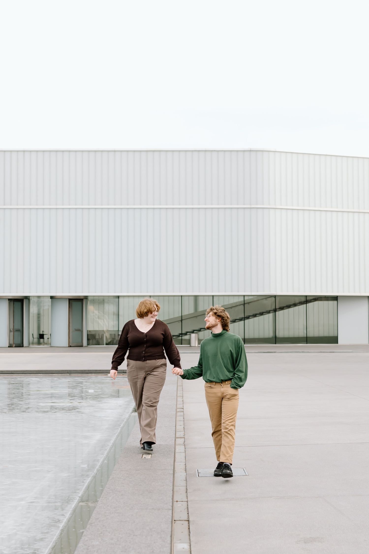 Two people walk together on a concrete ledge outside a modern white building with glass windows.