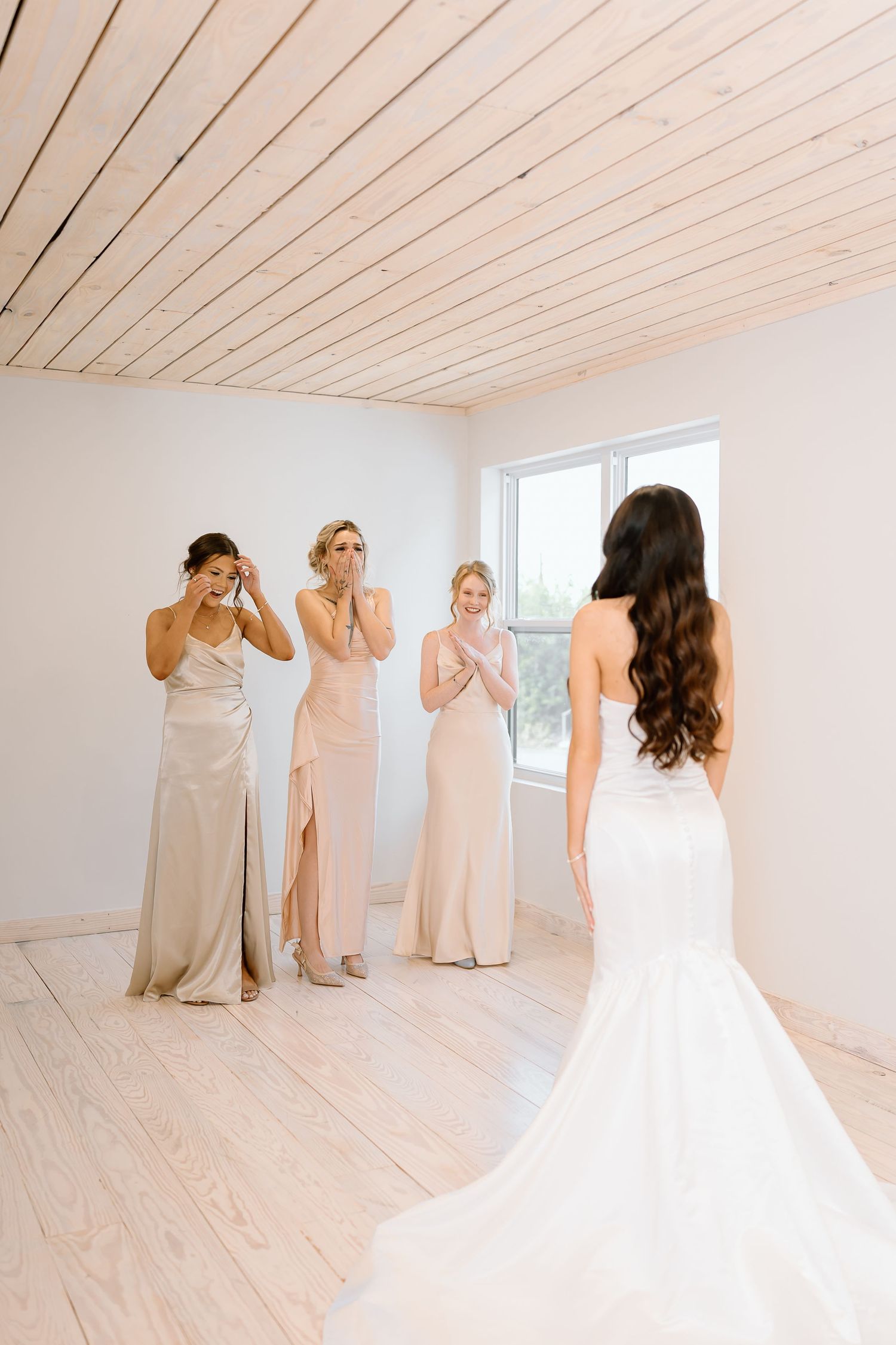 Bridesmaids in blush and champagne dresses share a first look with bride in white gown in bright studio setting.