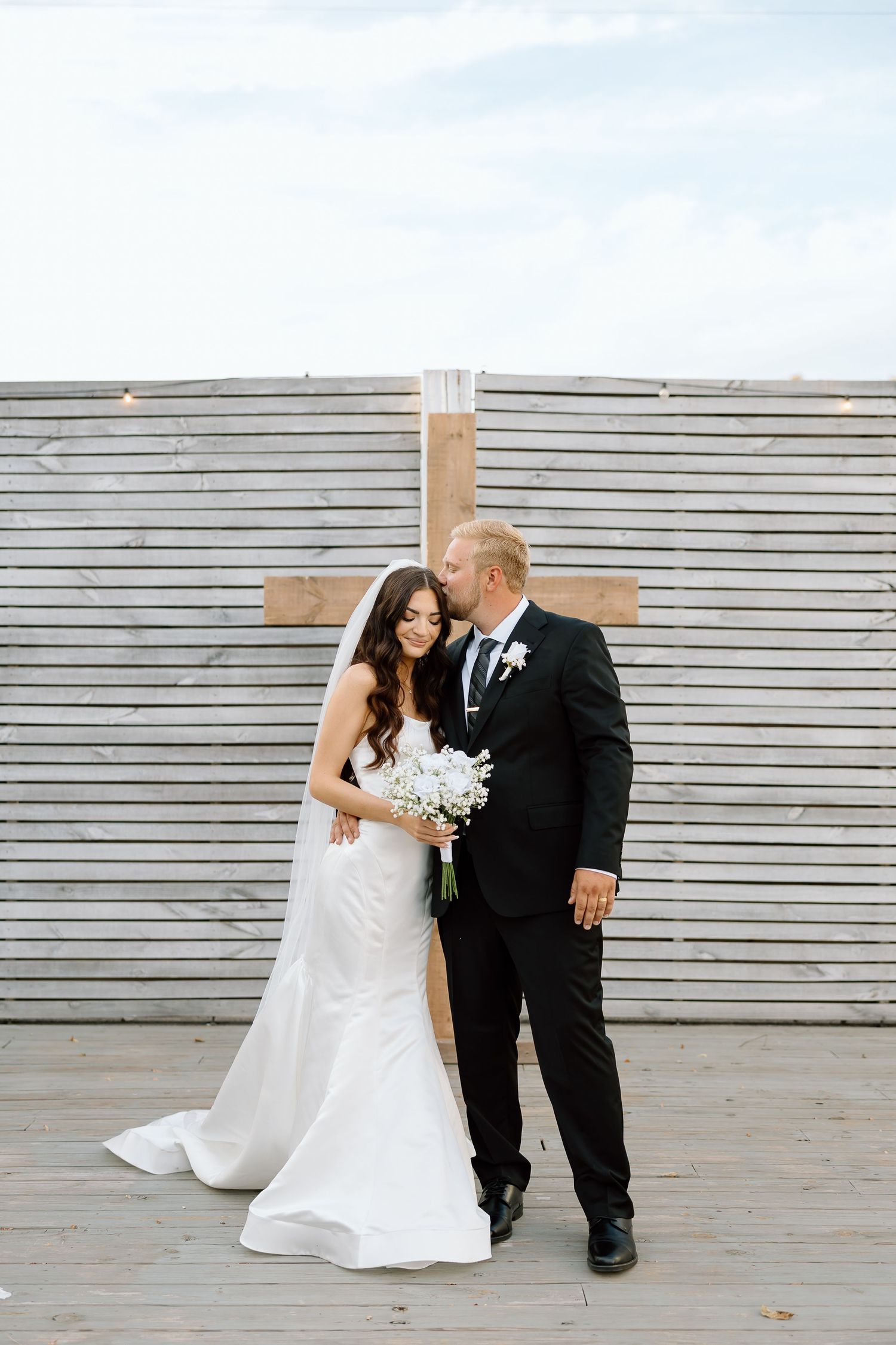A couple in wedding attire share intimate moments against a gray wall in a series of candid photos.