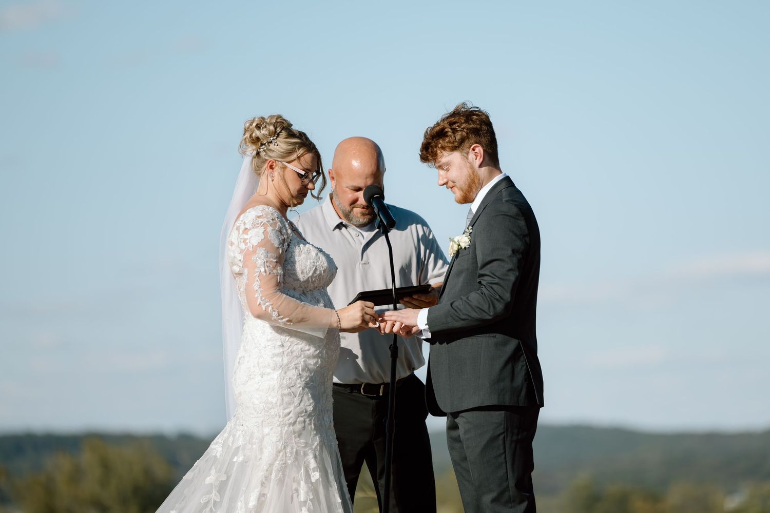 A couple exchanges rings during an outdoor wedding ceremony with mountains and blue sky in the background.