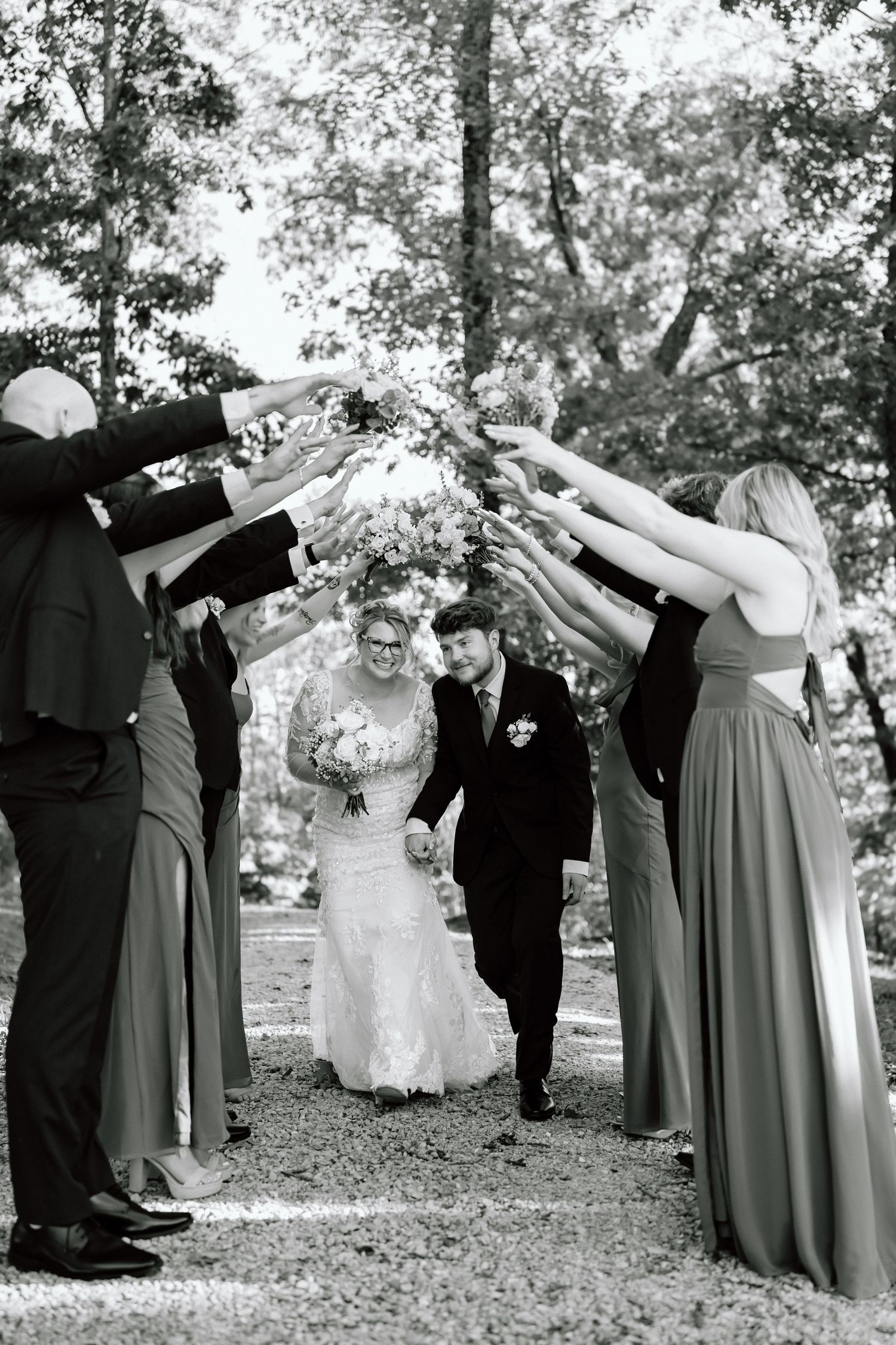 Wedding party poses in a fun sequence of dance moves under trees in black and white photography.
