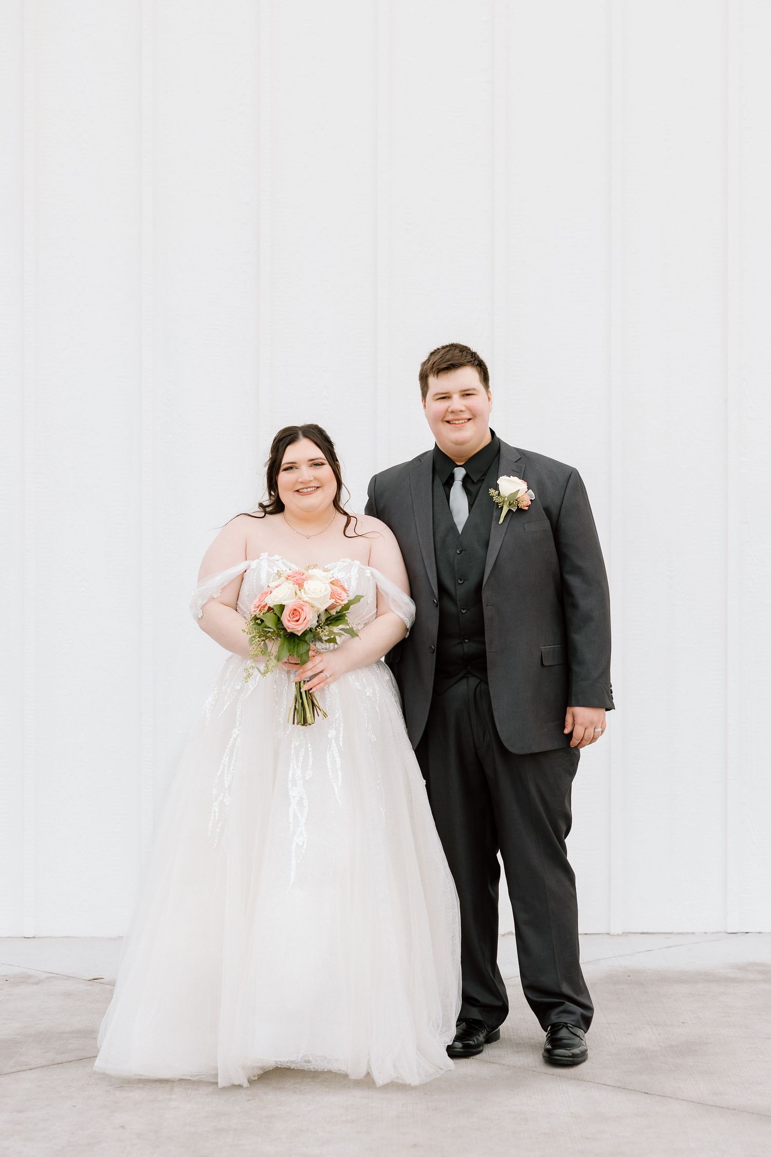 A wedding couple in formal attire poses against a white wall in a series of romantic portraits.