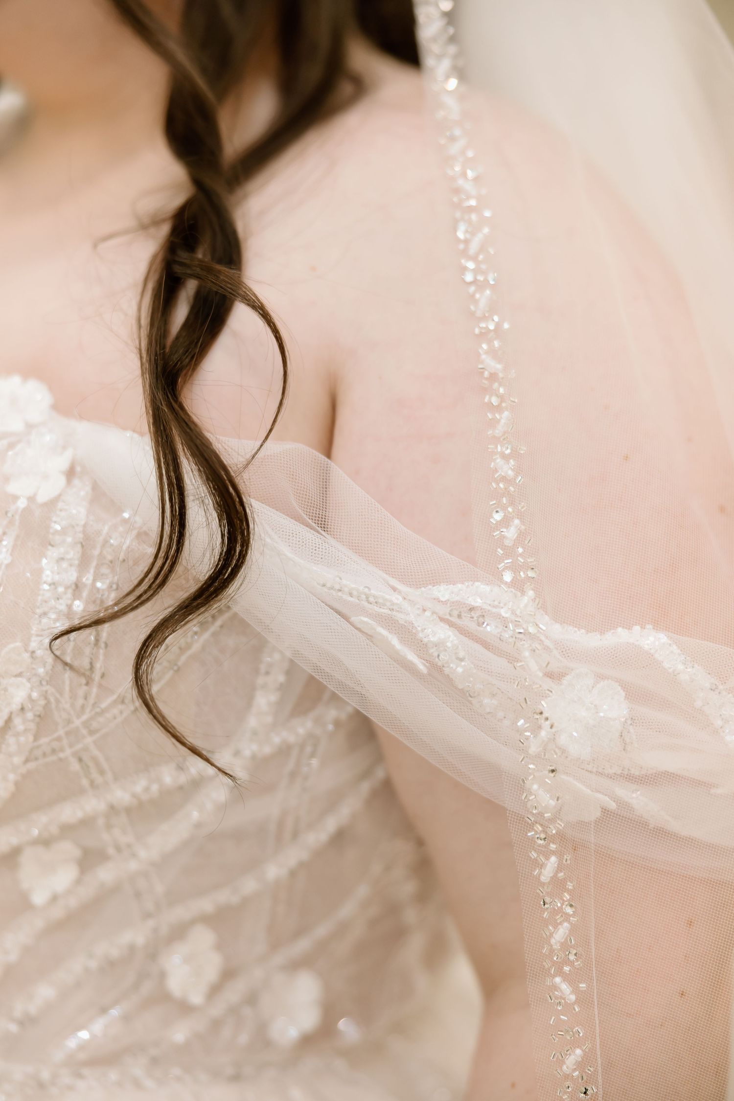 Close-up details of a delicate white lace wedding dress with pearl embellishments and soft curled hair.