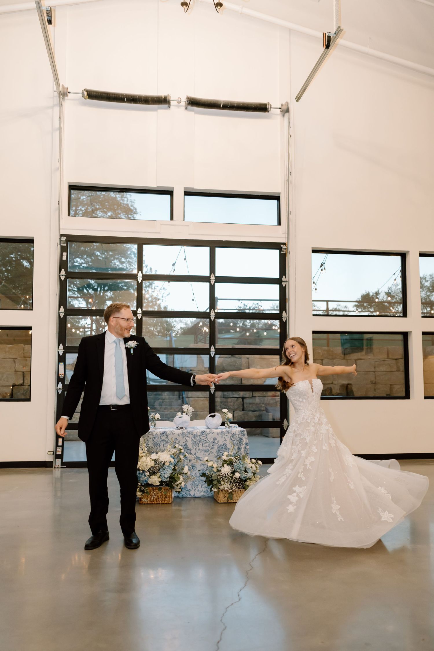 Bride and groom share their first dance in an elegant venue with large windows and floral decorations.