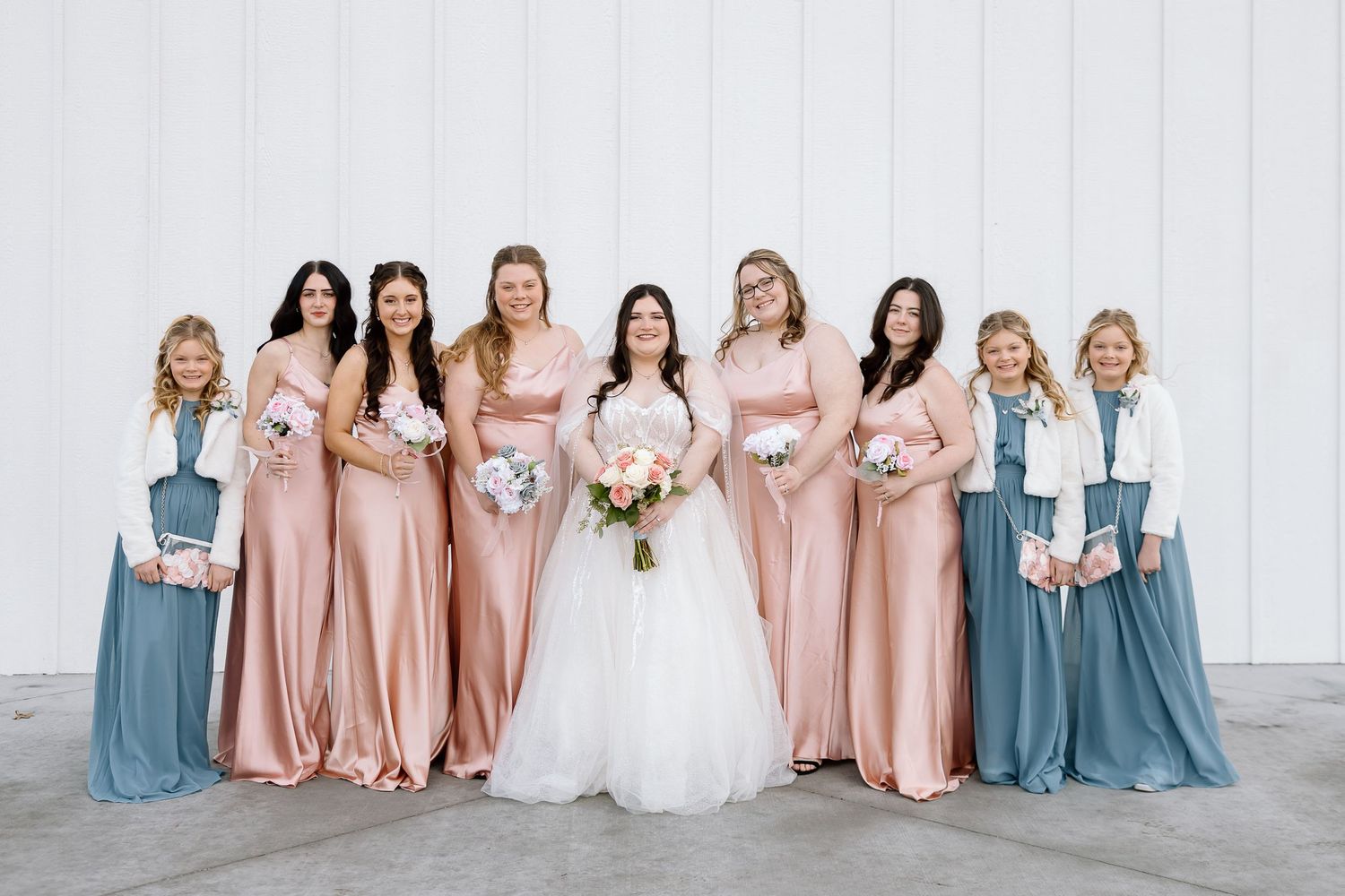 Bridal party wearing mix of pink and blue satin dresses lined up for formal photo.