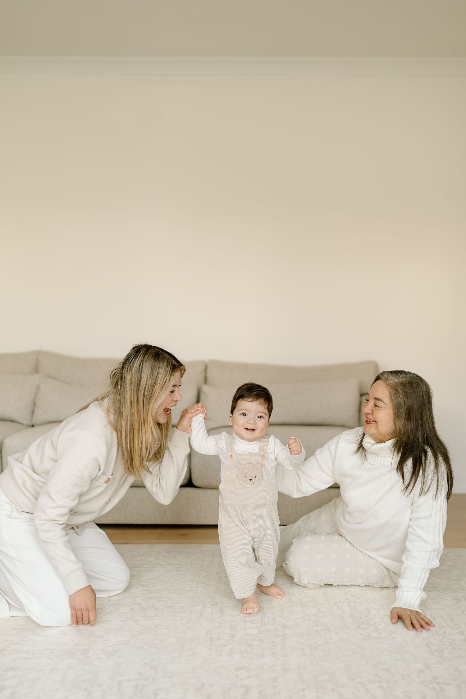 A series of five connected photos showing playful family interaction in white clothing on a light carpet.