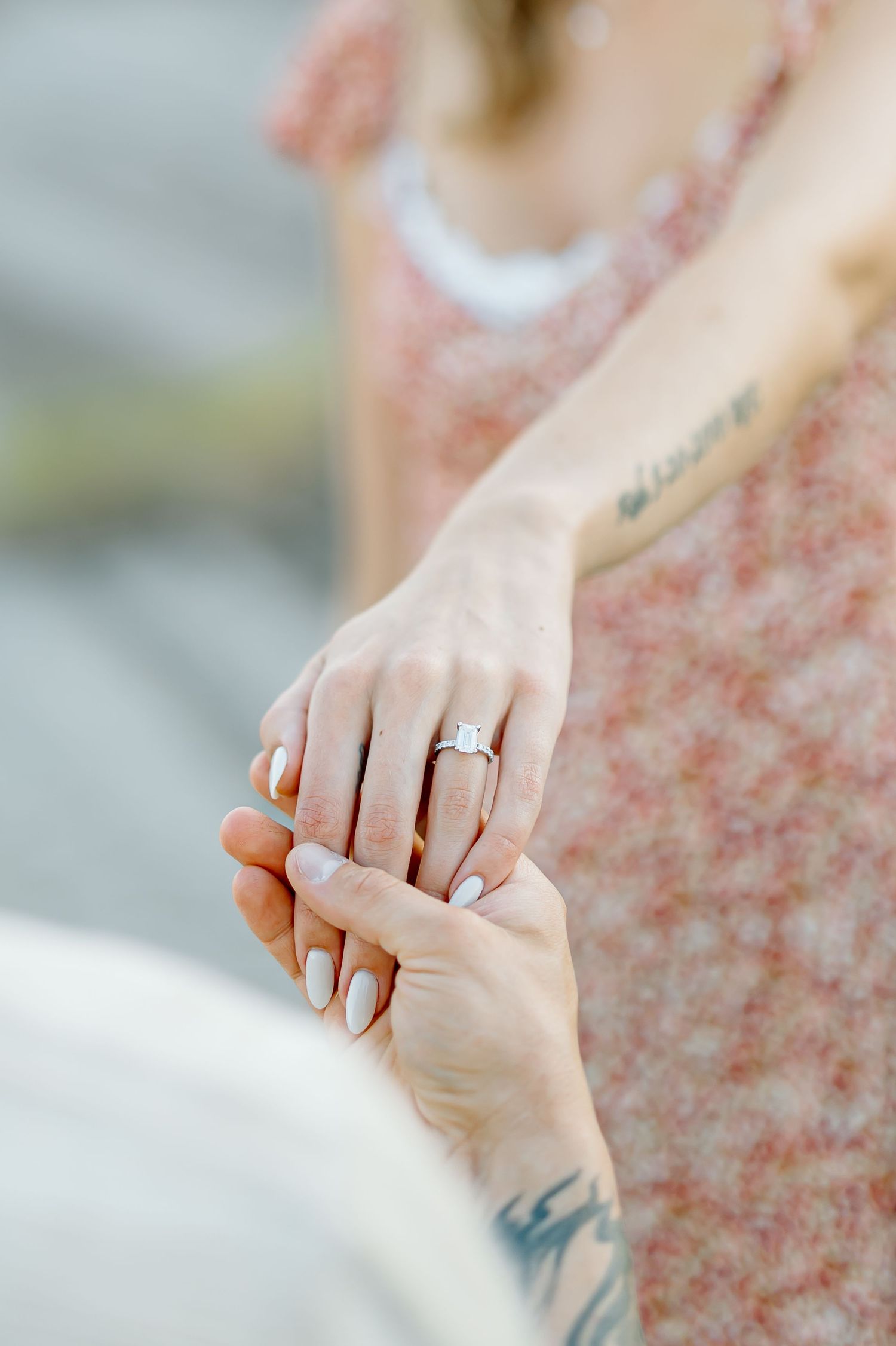 Close-up view of hands wearing engagement ring against a soft pink floral background.