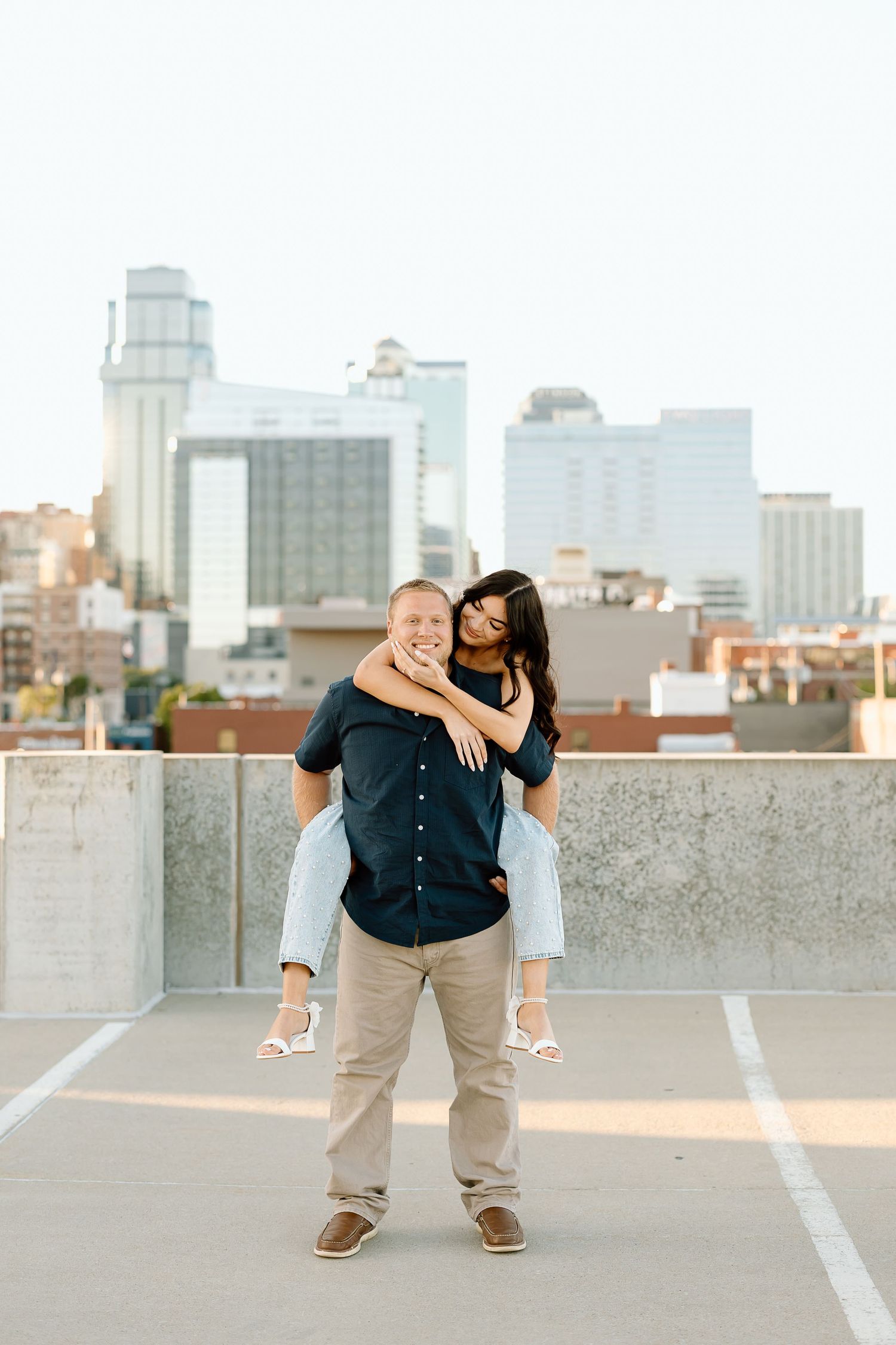 A couple shares playful and romantic moments together on an urban rooftop with a city skyline in the background.