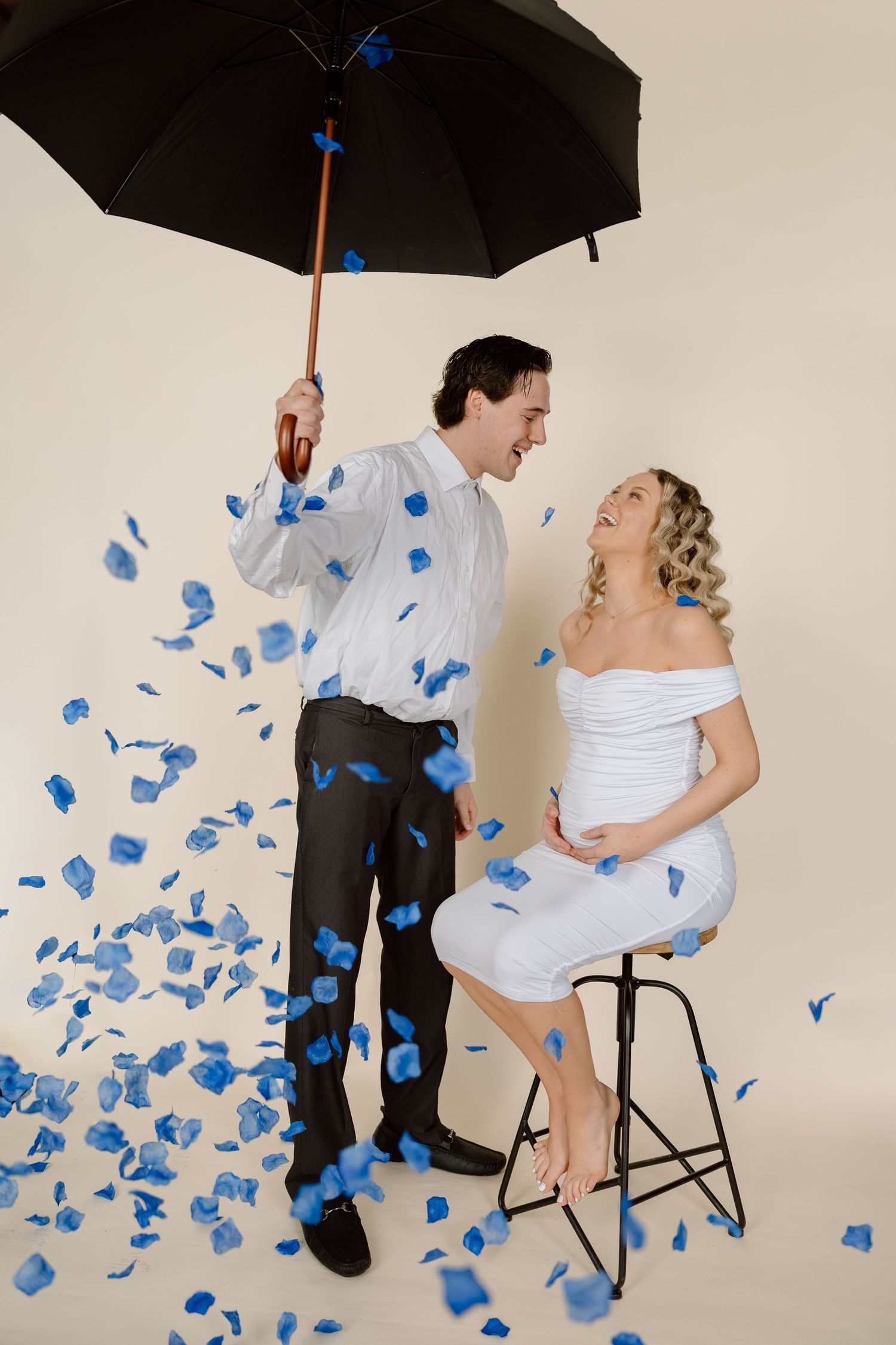 Artistic studio photo with black umbrella and swirling blue paper confetti against white backdrop in joyful celebration scene.