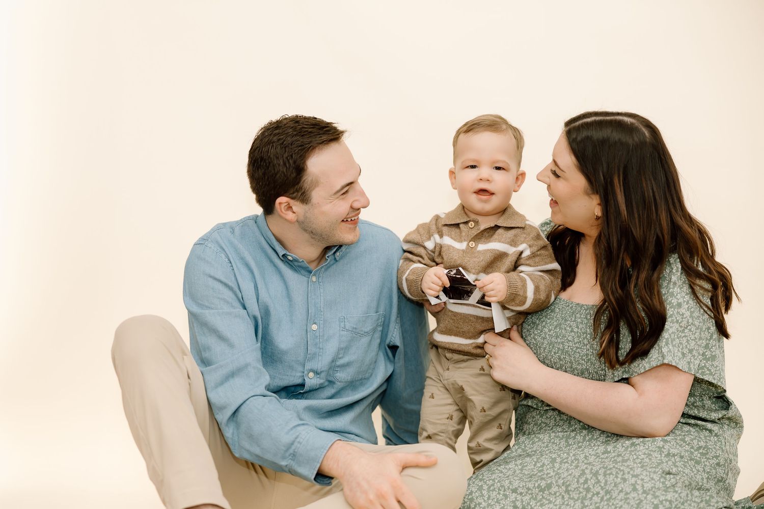 A family sits together on a light colored carpet in a casual indoor setting.