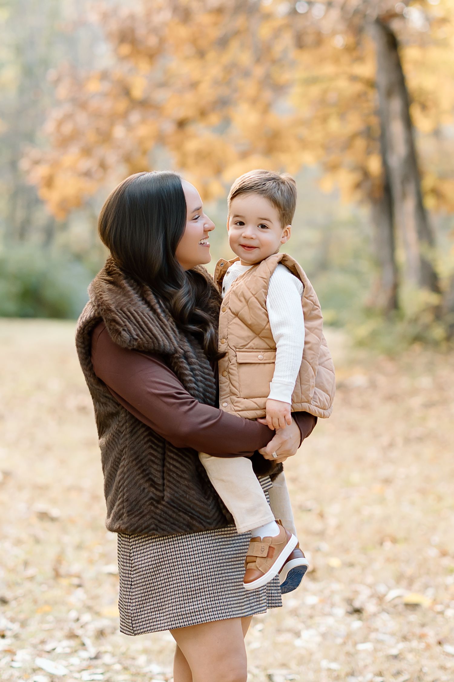 A parent and child share tender moments together during an autumn photoshoot with fallen leaves in the background.