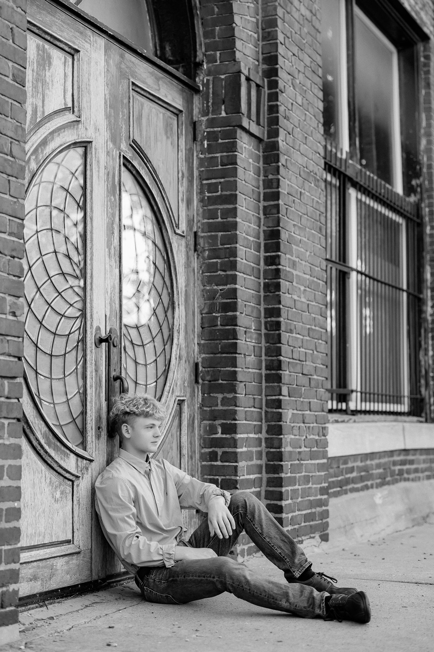 A person sits on the ground against a brick building with an ornate circular door design in black and white.