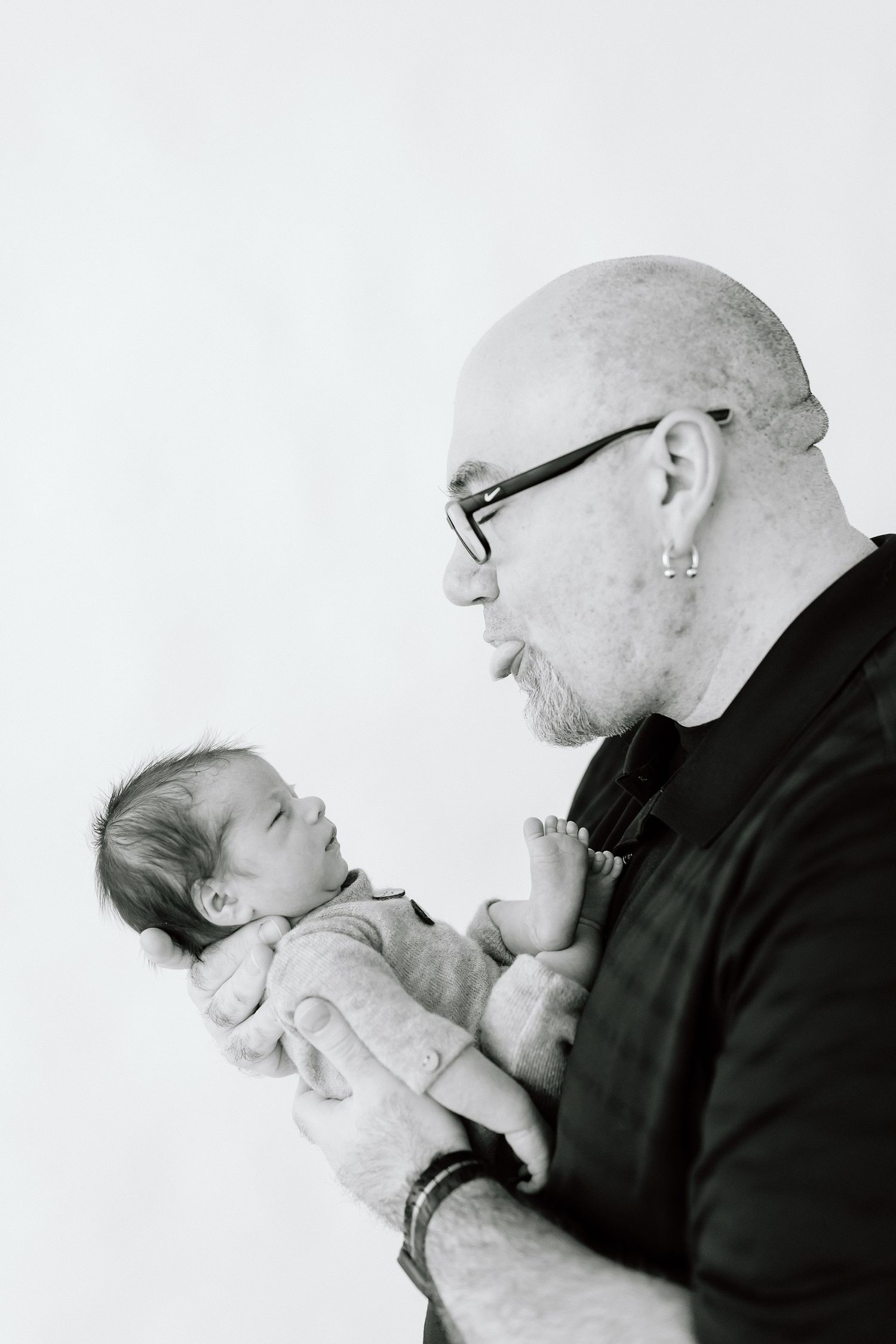 Black and white photo series showing tender moments between a parent in dark clothing holding a small infant.