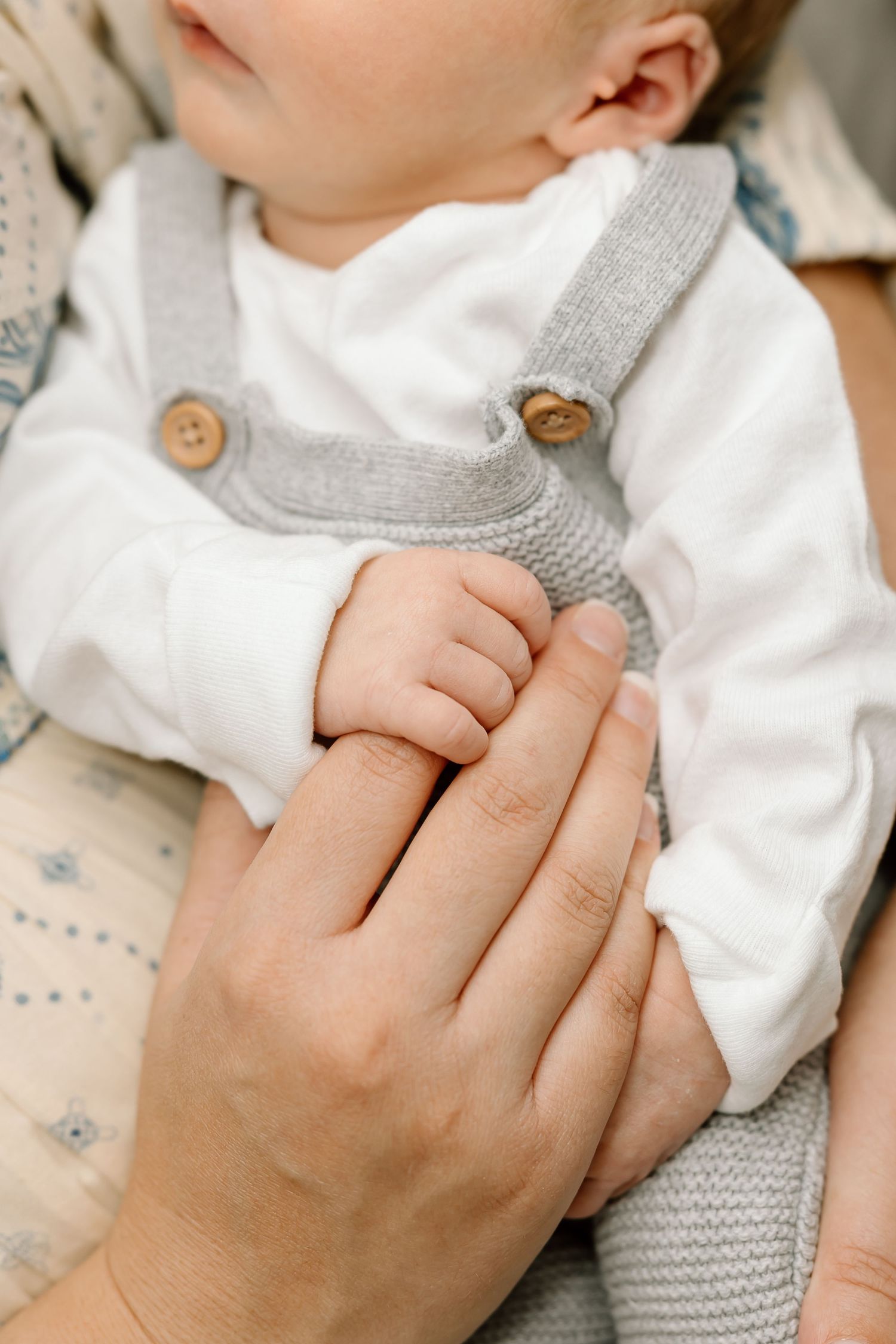 Close-up series of gentle hands holding a baby wearing a white and gray outfit with buttons.