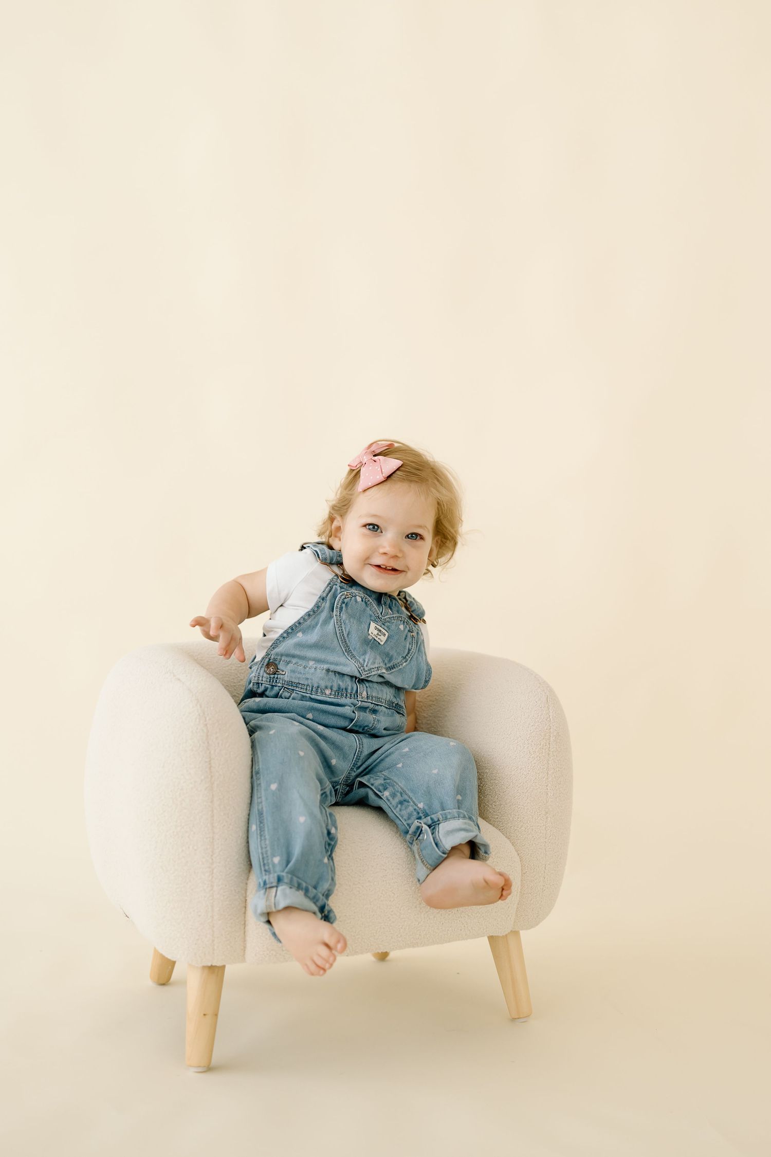 Three sequential photos show a baby in denim overalls lounging on a small white modern chair against a neutral backdrop.