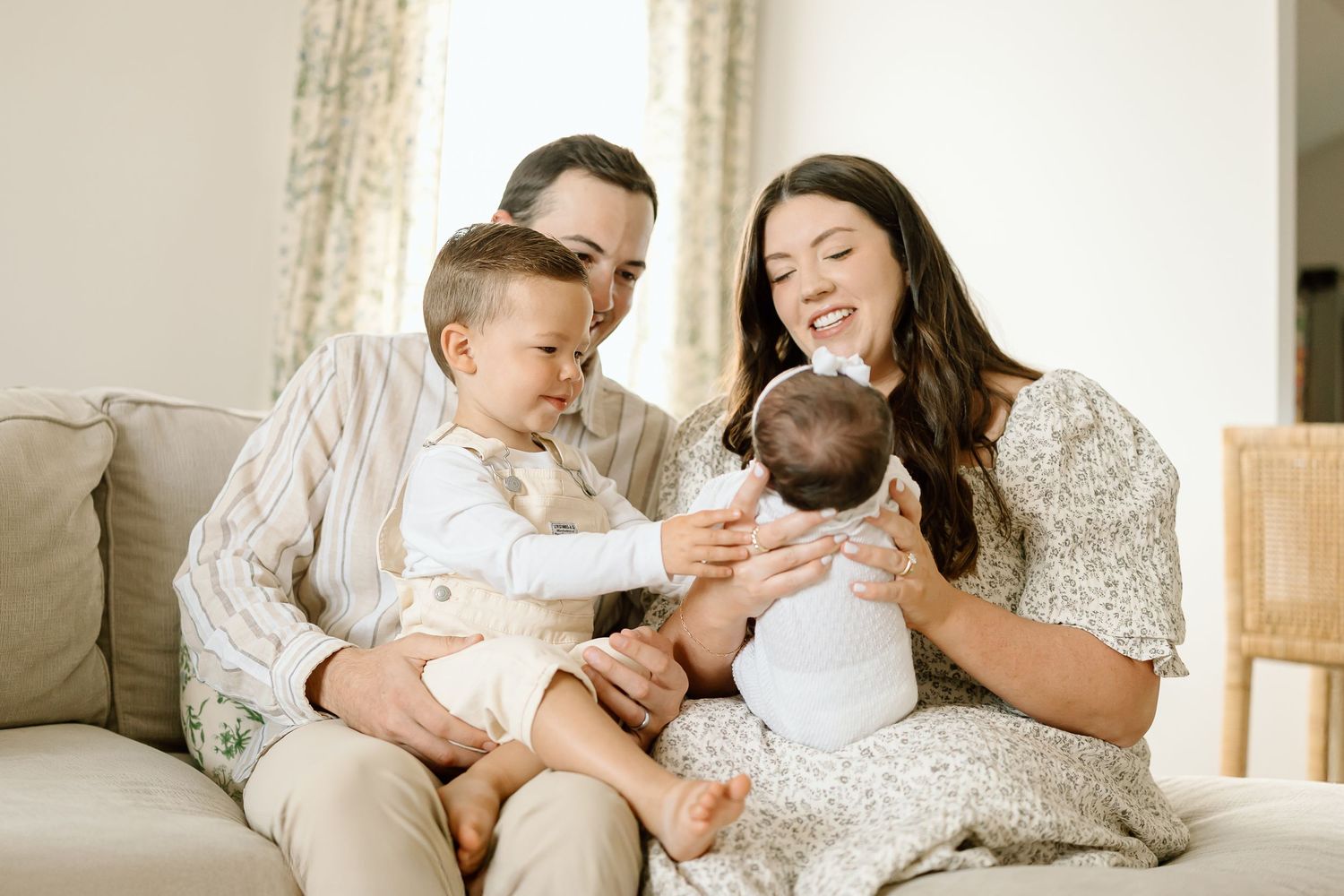 A happy family sits together on a beige couch in a bright living room sharing joyful moments.