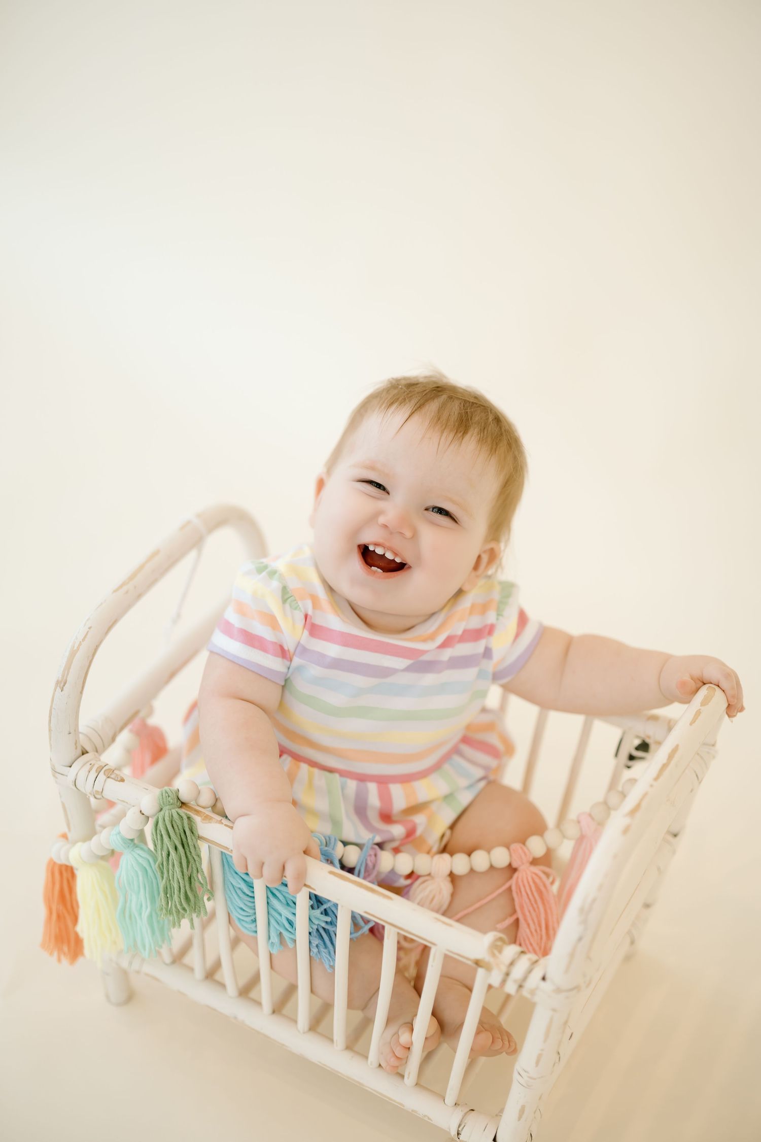 Colorful series showing a joyful baby playing in a small white wooden doll bed with rainbow tassels.