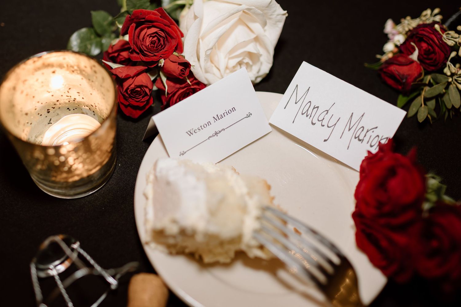 Wedding place cards and name cards are elegantly displayed alongside deep red roses and white floral arrangements.