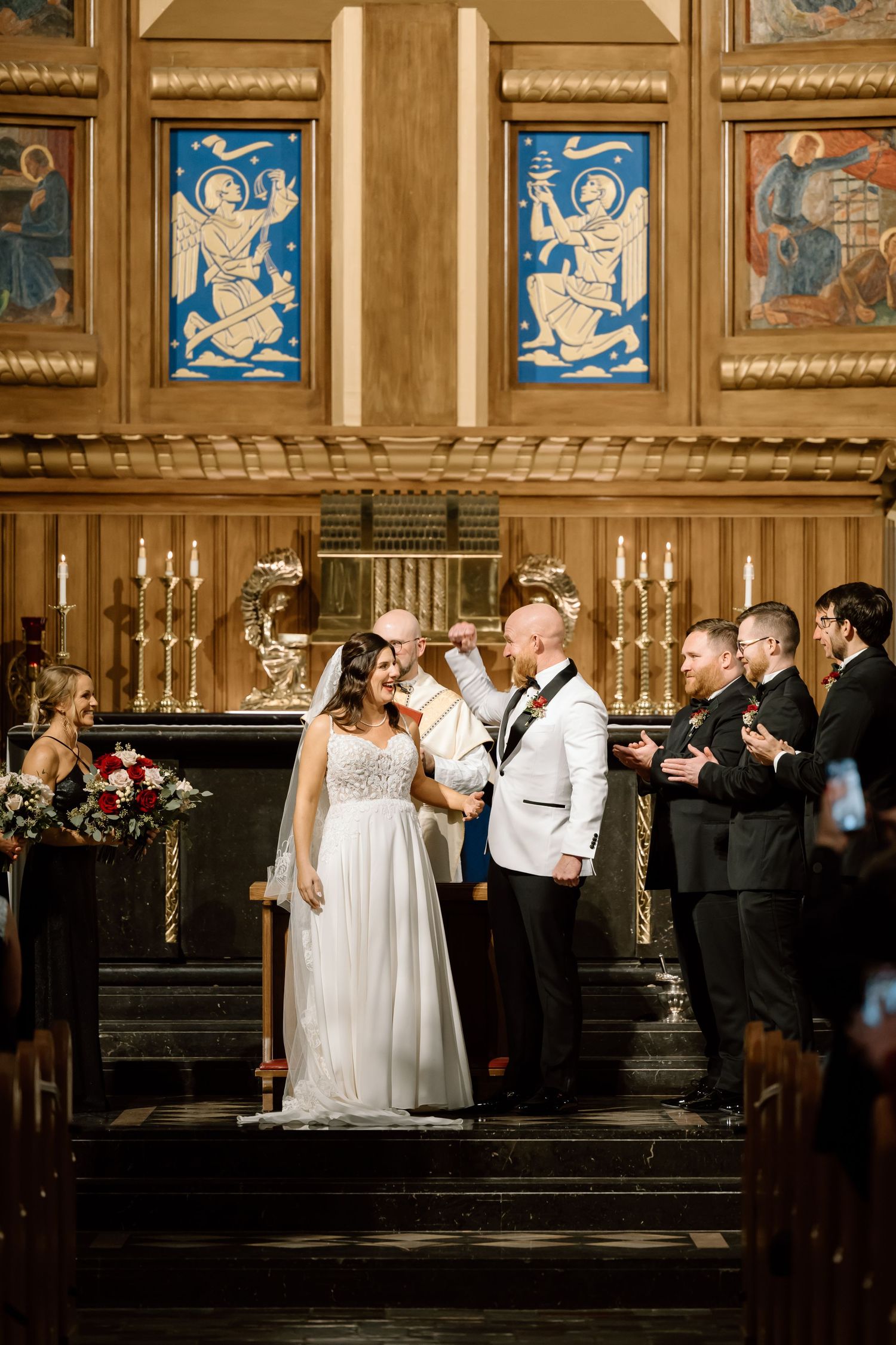 A wedding ceremony takes place in an ornate church with stained glass windows and golden decor at the altar.