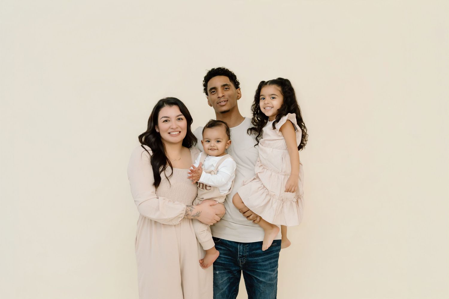Family wearing coordinated pink and white outfits poses together against neutral background.