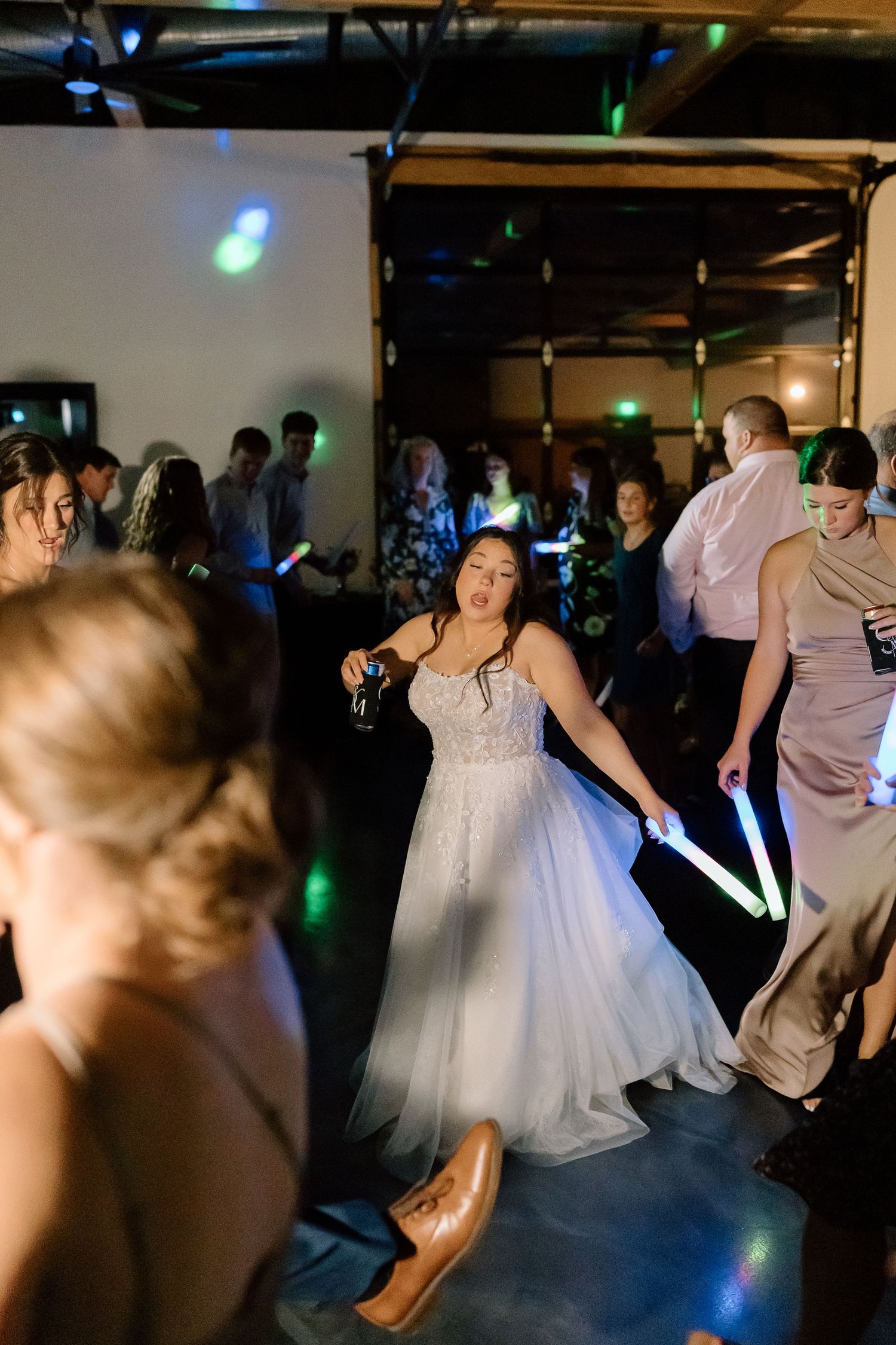 Wedding guests dance together on a dimly lit dance floor with blue and green lighting effects during an evening reception.