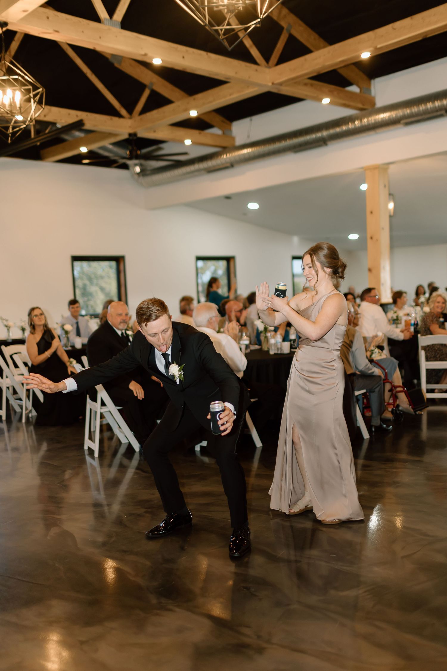 Wedding guests dance and celebrate on a polished concrete floor in an elegant venue with exposed wooden beams.