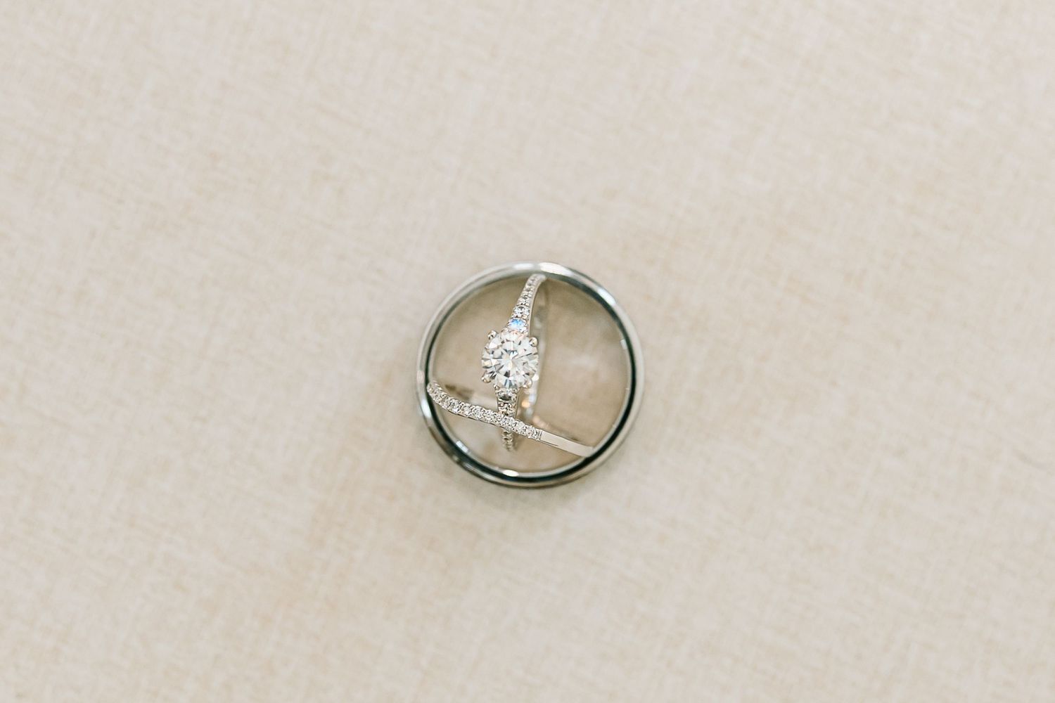 Wedding rings arranged on a beige surface with one ring featuring a sparkling diamond solitaire.