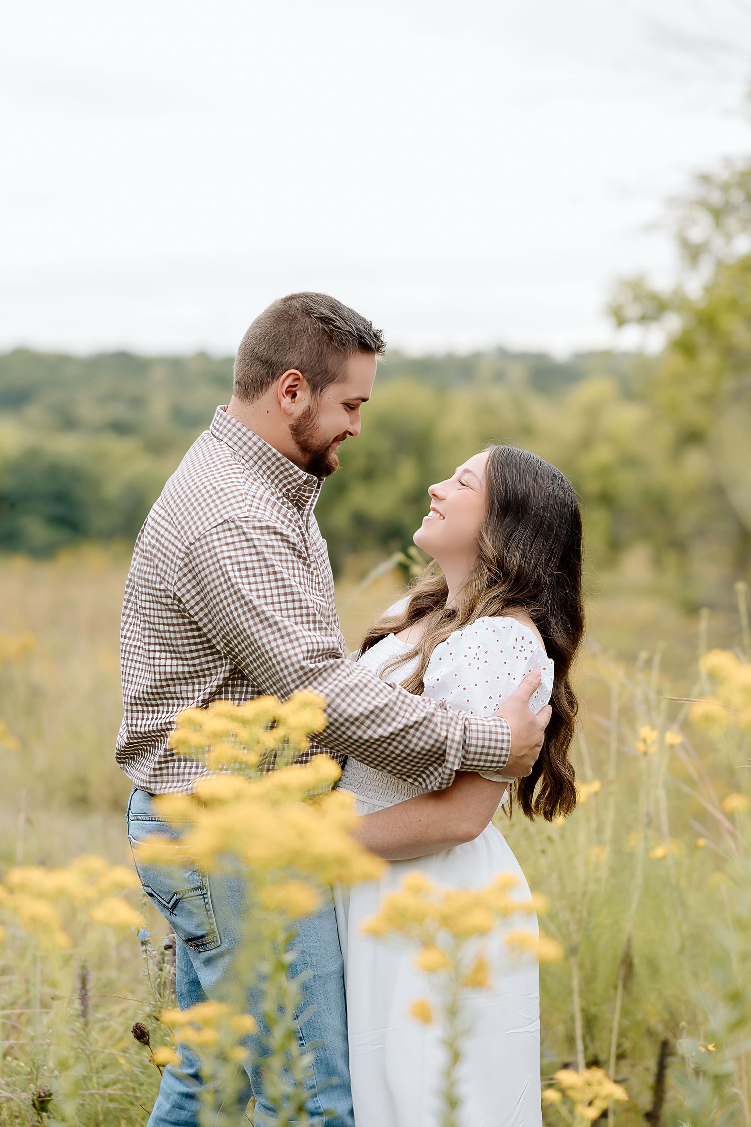 Playful moment between couple laughing together in field of yellow summer wildflowers.