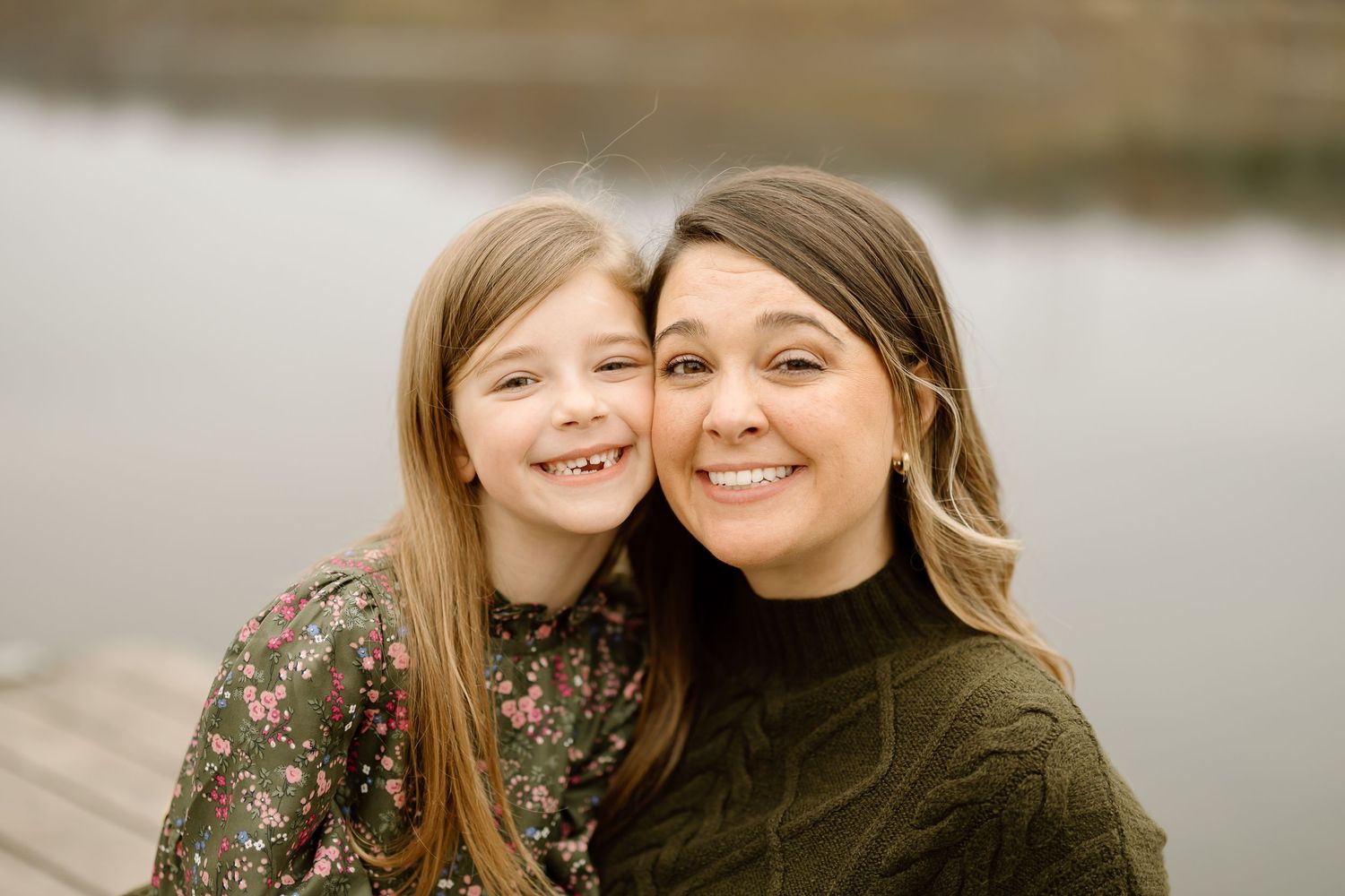 Parent and child share joyful embrace during lakeside photo session on wooden dock.