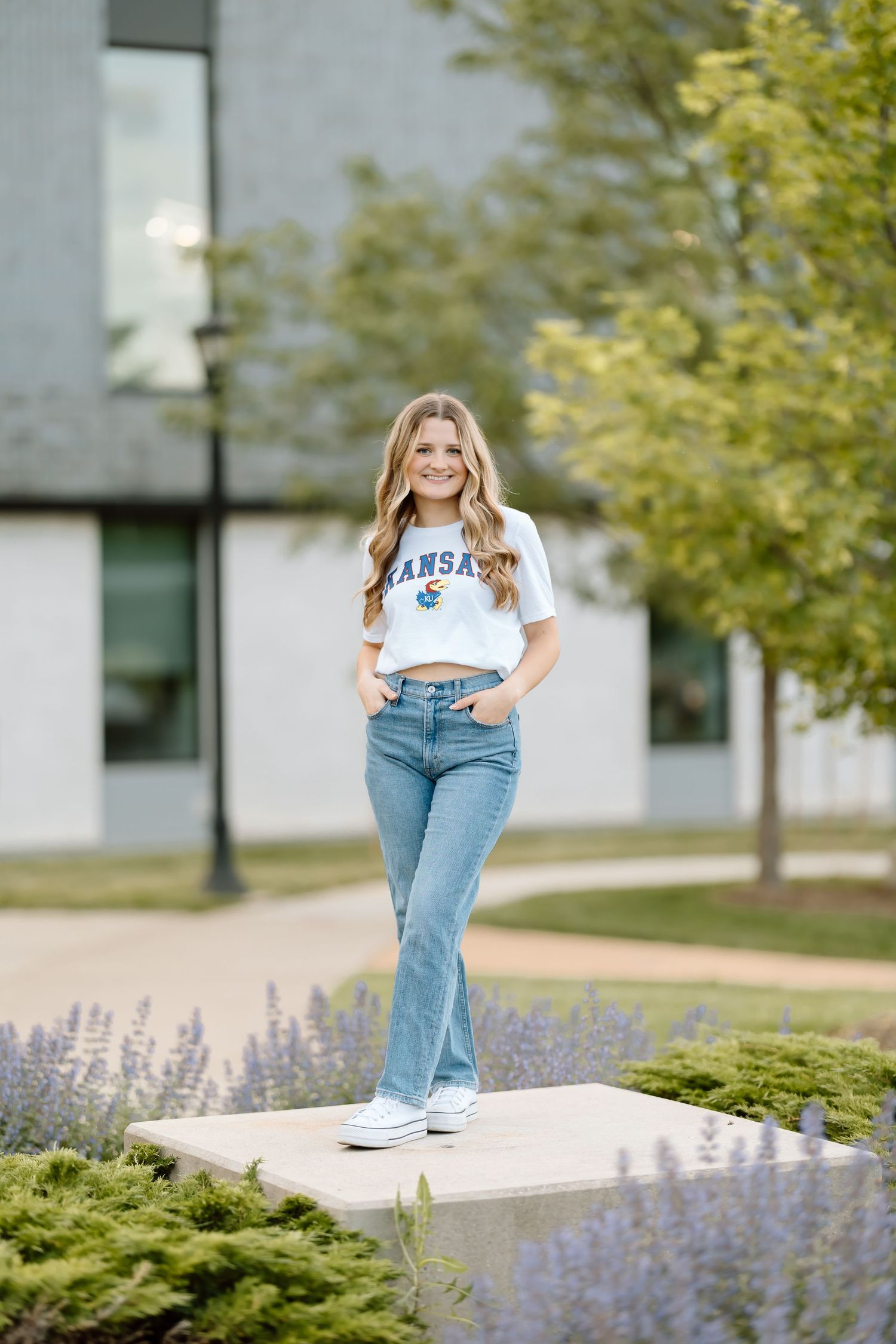 A person in a NASA t-shirt and jeans poses outdoors near lavender flowers and greenery on a sunny day.