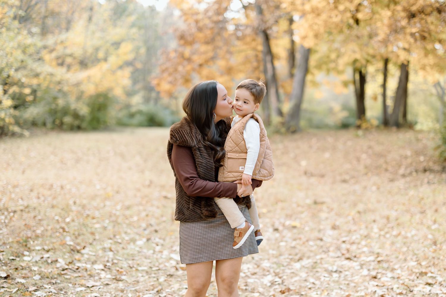 A parent and child share a tender moment together in a fall setting with golden leaves on the ground.