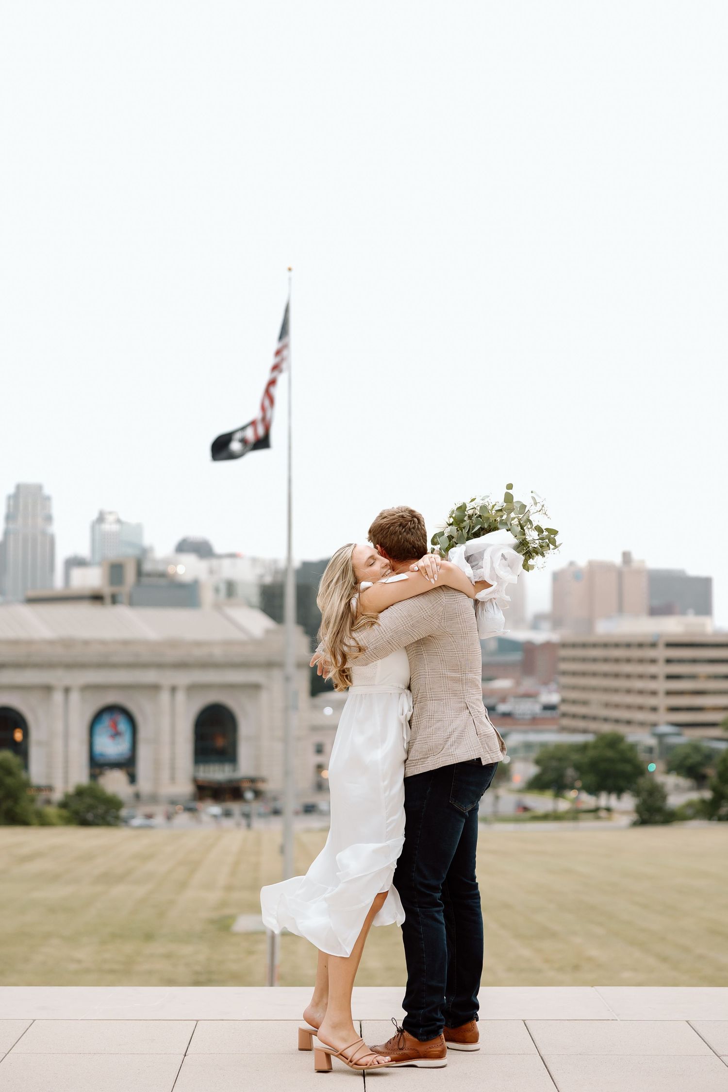A romantic couple embraces during a wedding photoshoot on a rooftop terrace with a cityscape backdrop.