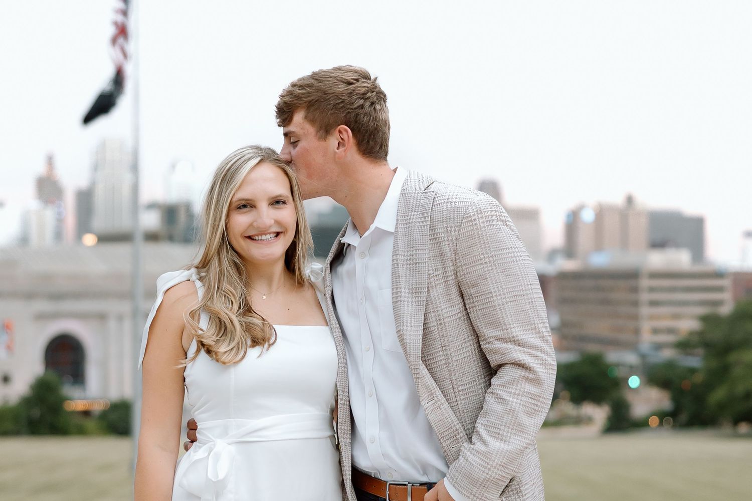 A couple in wedding attire poses for romantic photos with a city skyline in the background.
