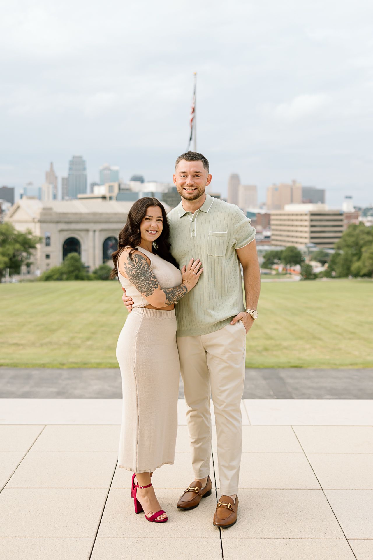 A couple poses together on a concrete plaza with a city skyline visible in the background.
