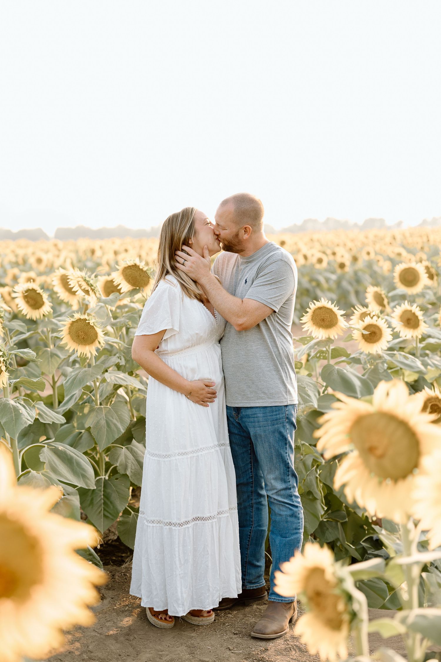 A couple shares a romantic moment in a golden sunflower field during sunset, creating a dreamy summer atmosphere.
