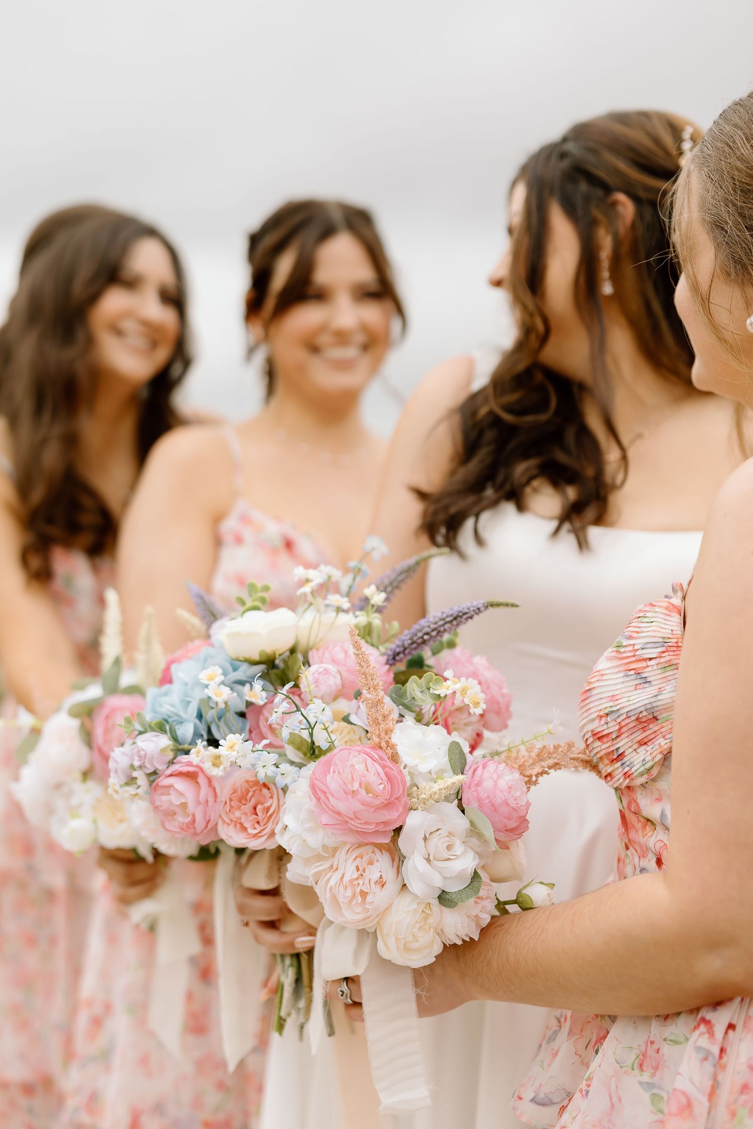 A line of bridesmaids holding romantic pink and white floral bouquets with roses and delicate greenery.