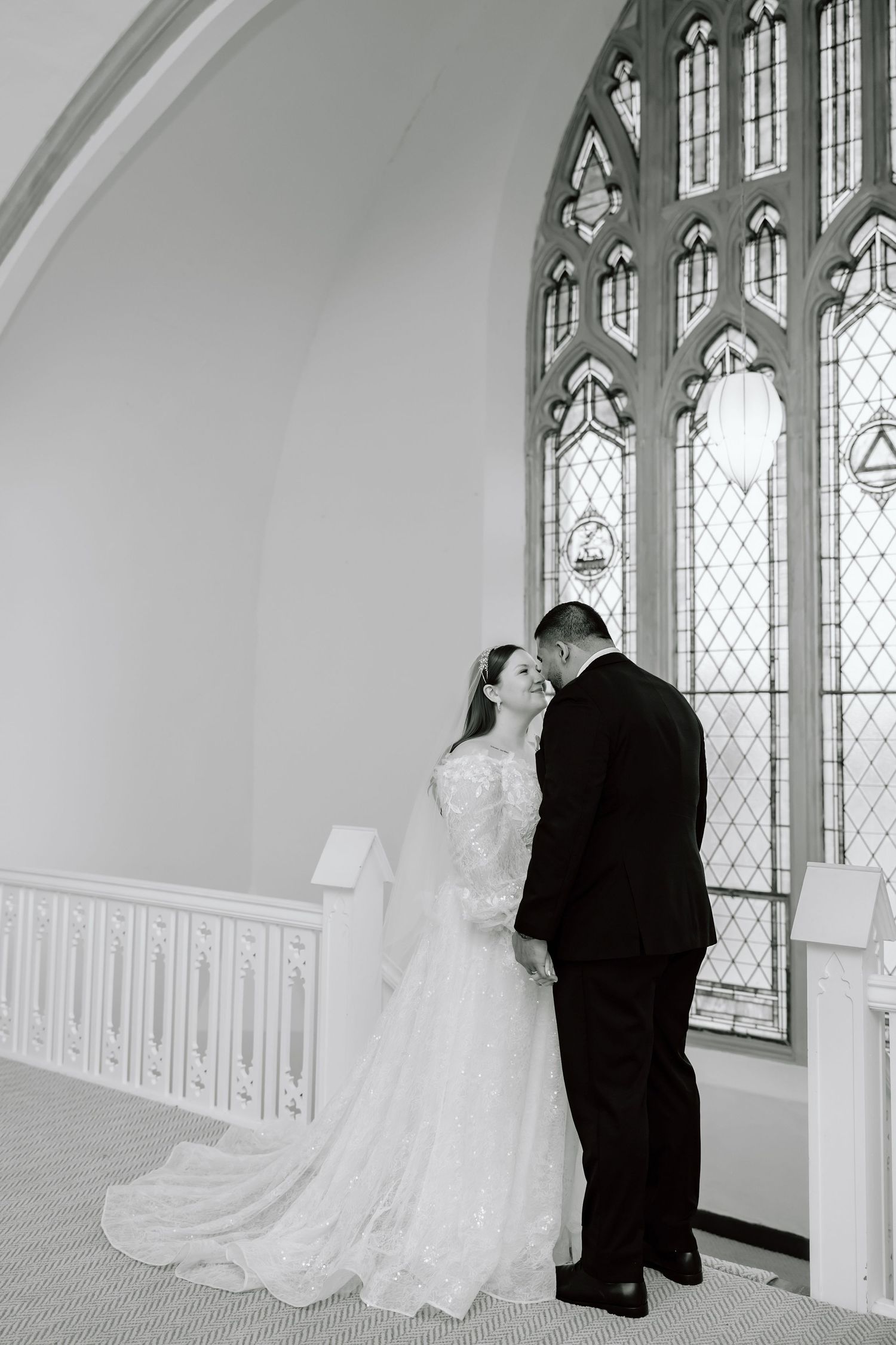 Black and white photo of bride and groom sharing an intimate moment before a stained glass window in a church.