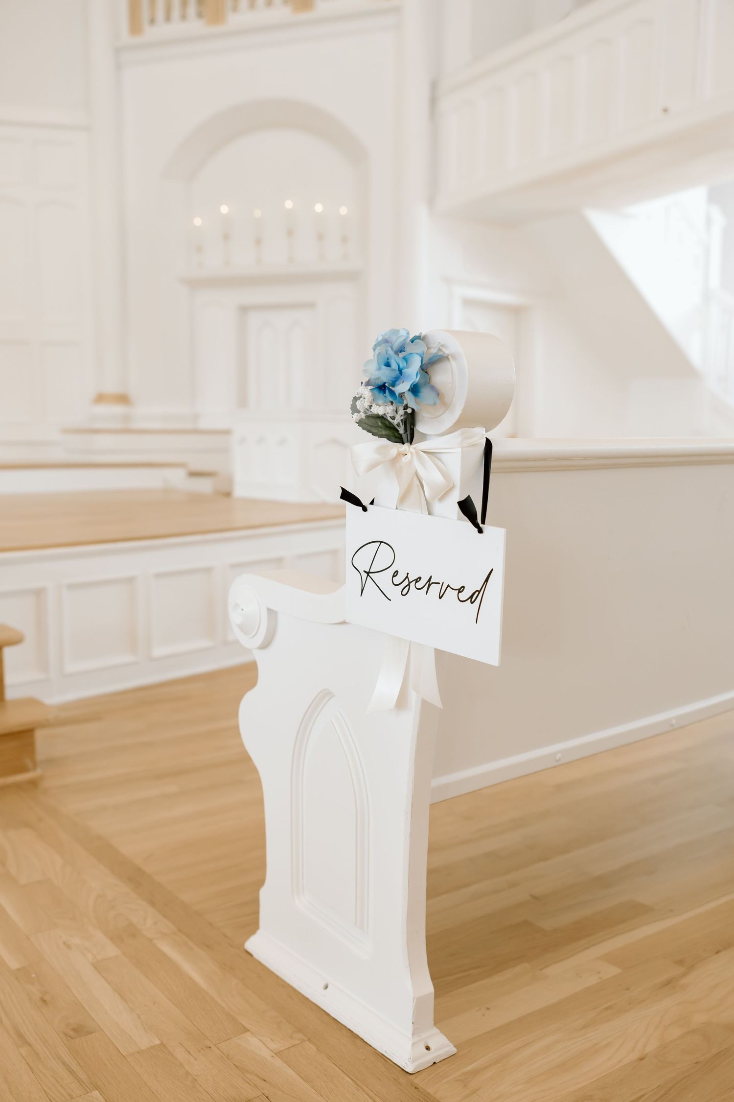 White church pew with Reserved sign and blue hydrangea floral decoration for a wedding ceremony.