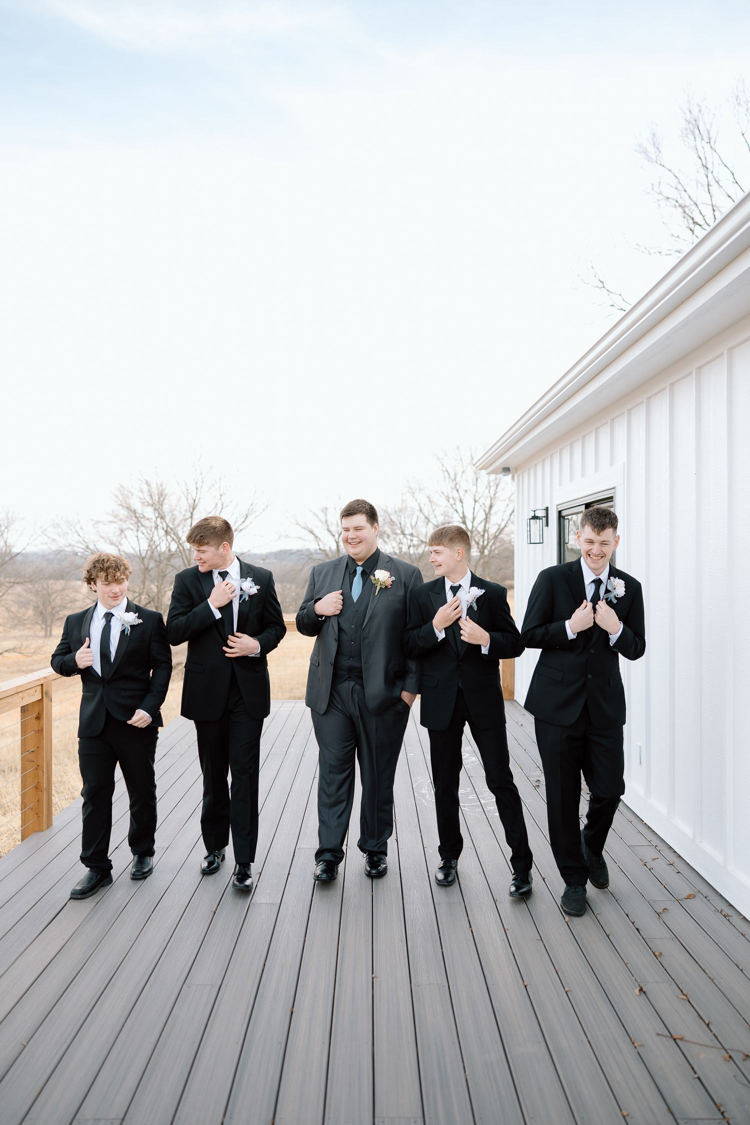 Wedding party members in black tuxedos line up and bow dramatically on a white deck in a fun photo sequence.