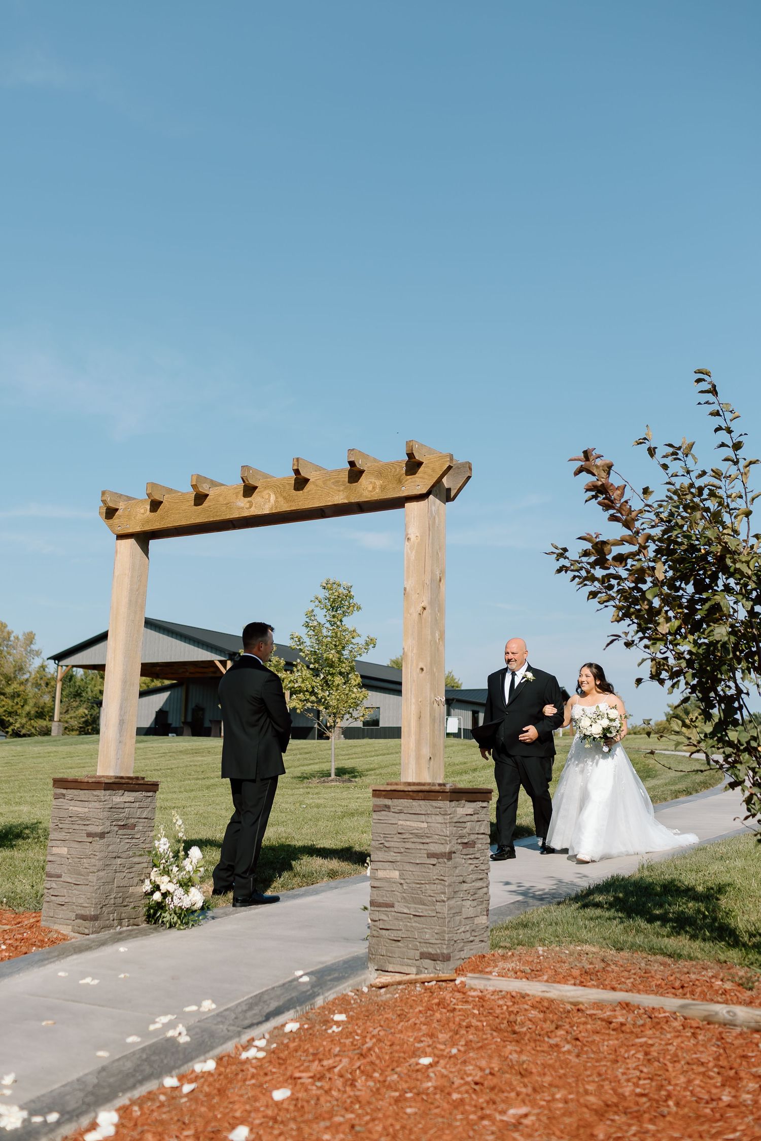 A series of outdoor wedding photos showing a couple walking under a wooden pergola with stone pillars at sunset.