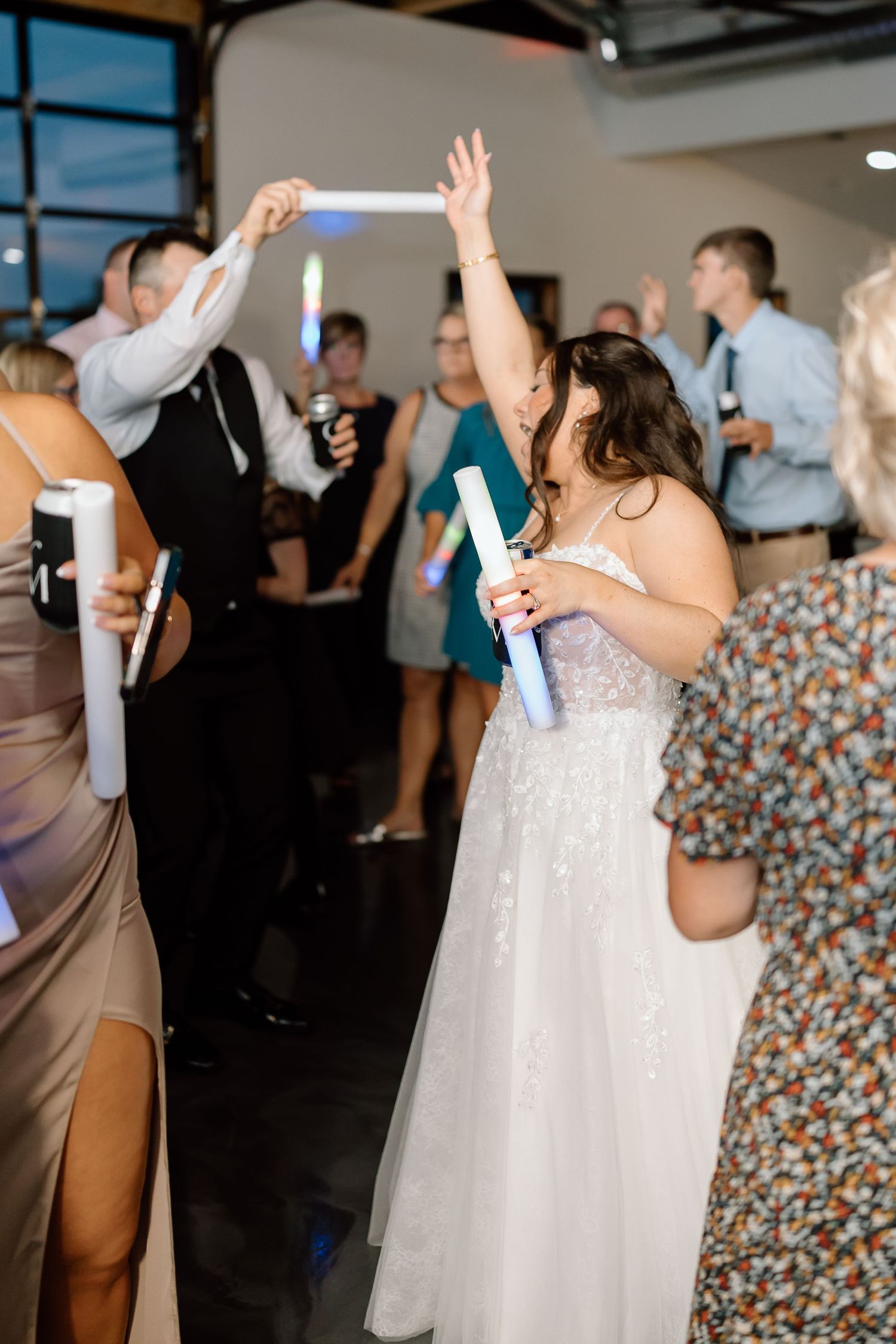 Wedding guests dance and celebrate on the dance floor while holding glowing light sticks during an evening reception.