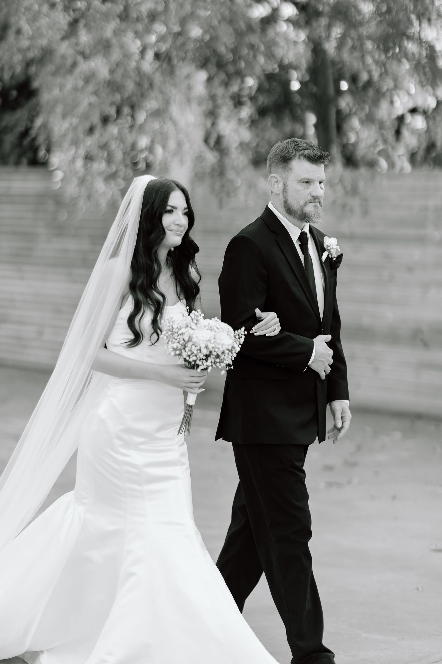 A bride and groom share a joyful moment walking together outdoors in black and white photography.