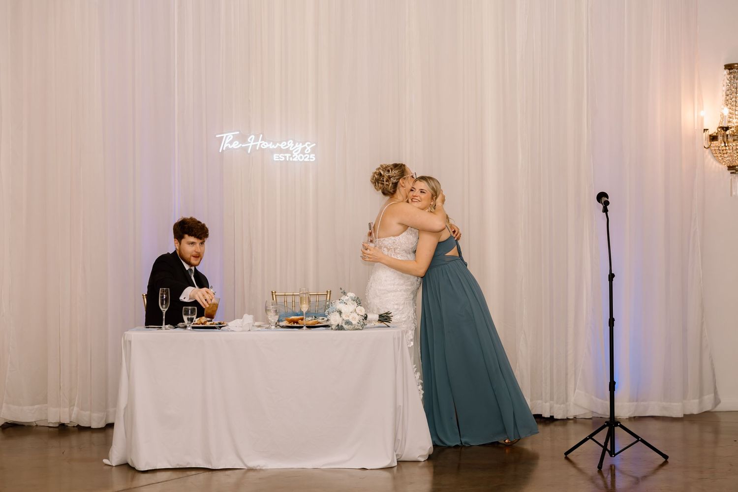 A wedding reception venue with white drapes, elegant lighting, and a dance floor setup.