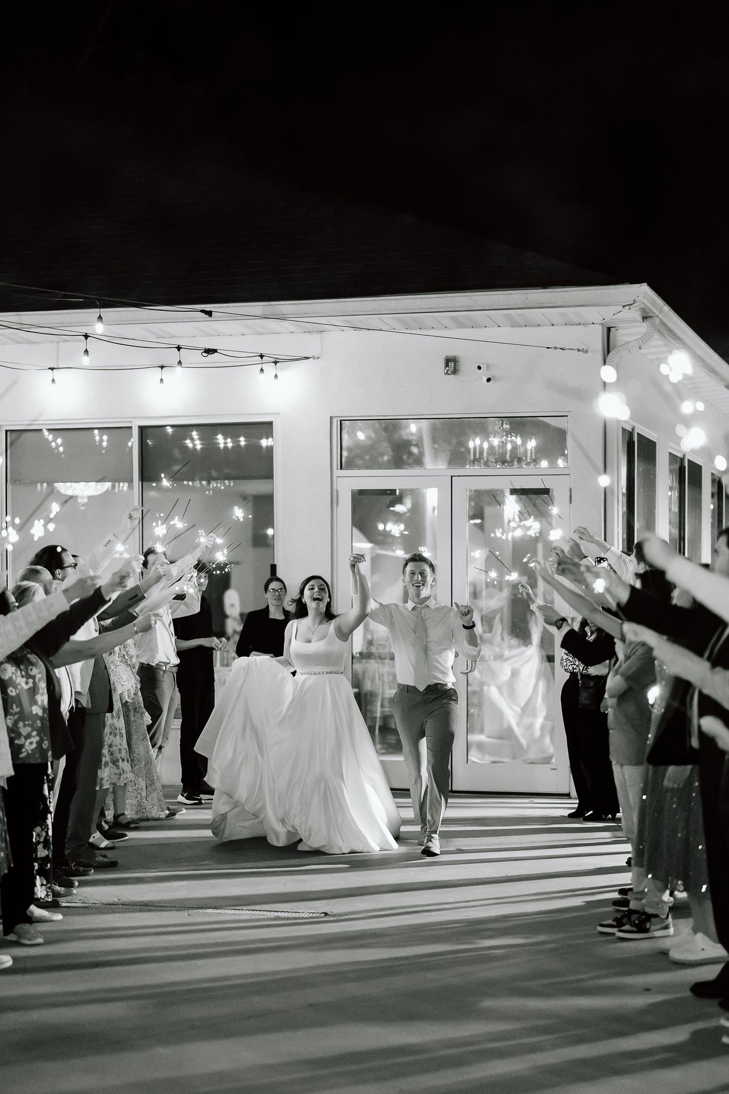 A sequence of black and white photos showing a wedding couple exiting through a sparkler sendoff line at night.